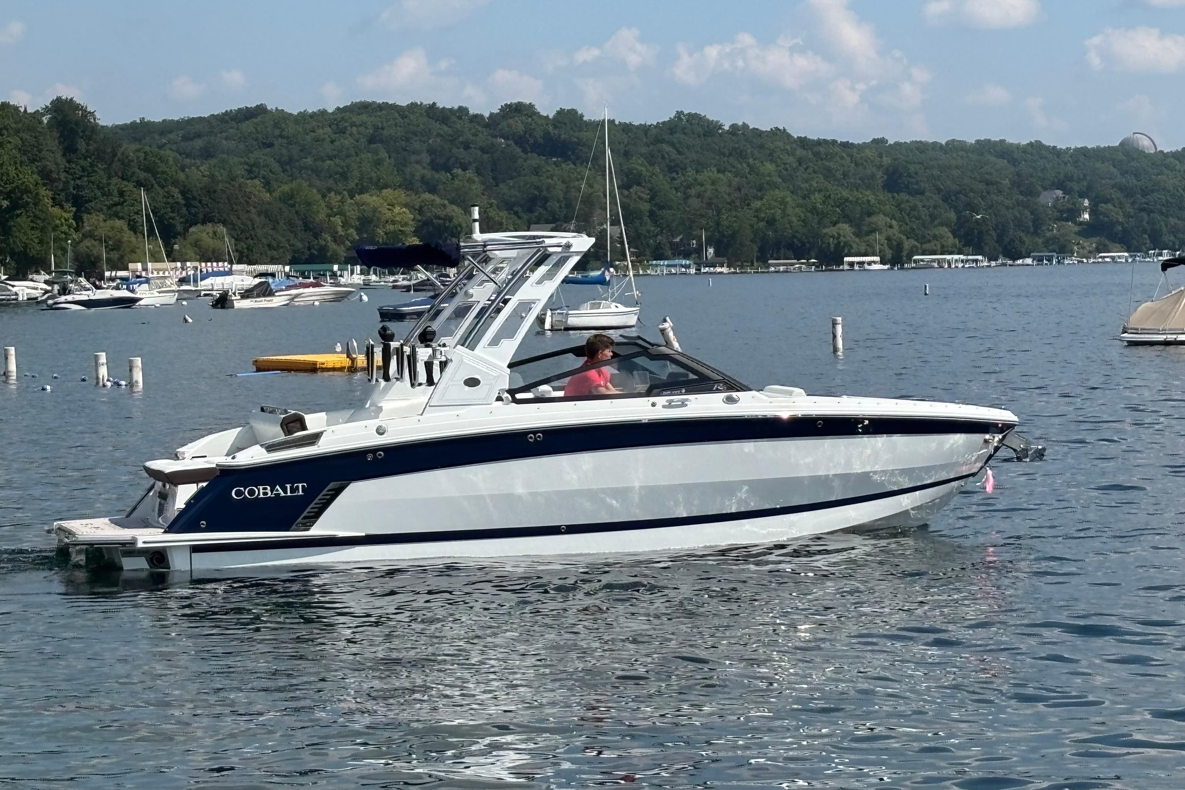 2025 Cobalt R6 Surf boat cruising on a scenic lake with lush green shoreline.