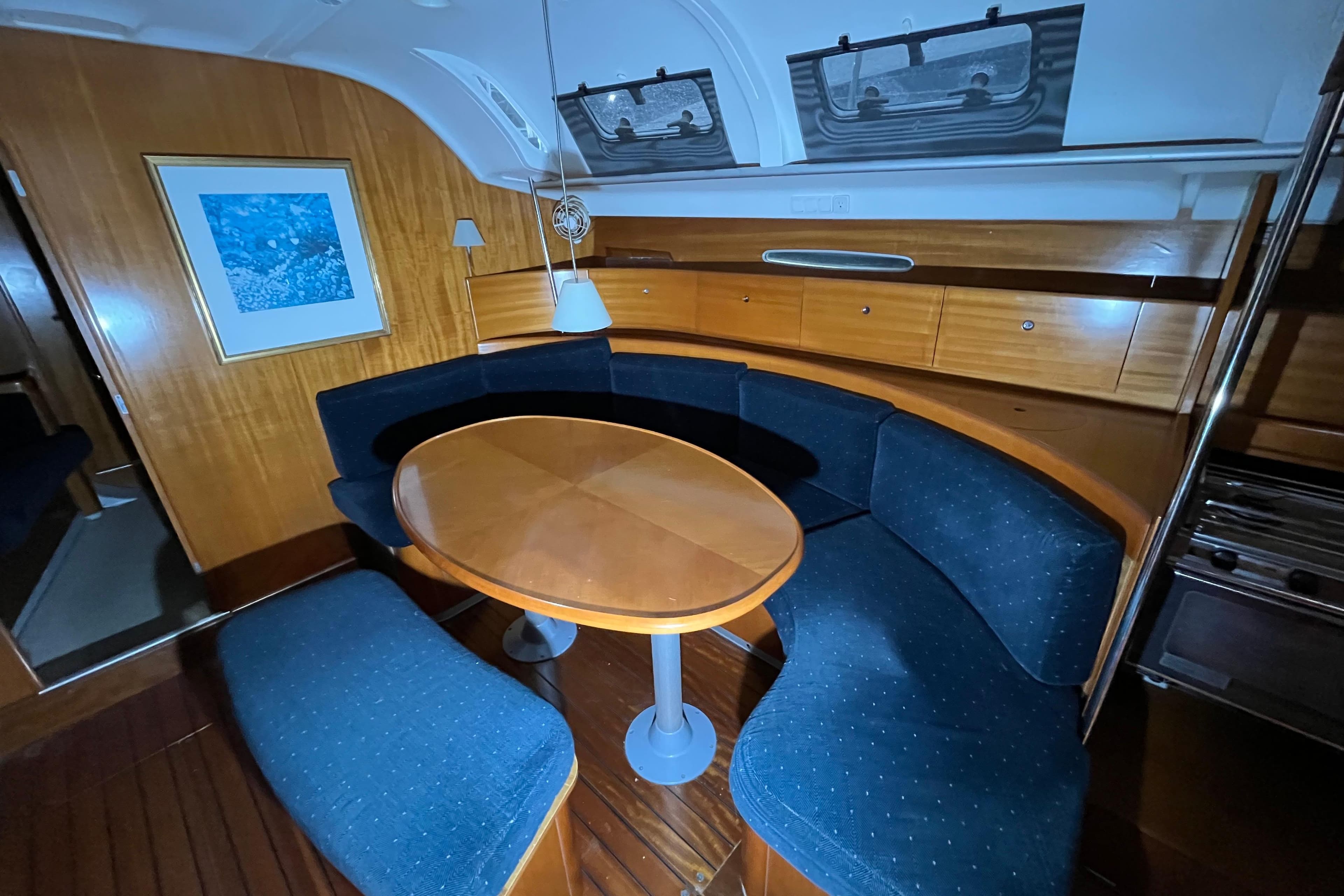 Interior of 1999 Beneteau First 42s7 yacht with curved seating and wooden table.