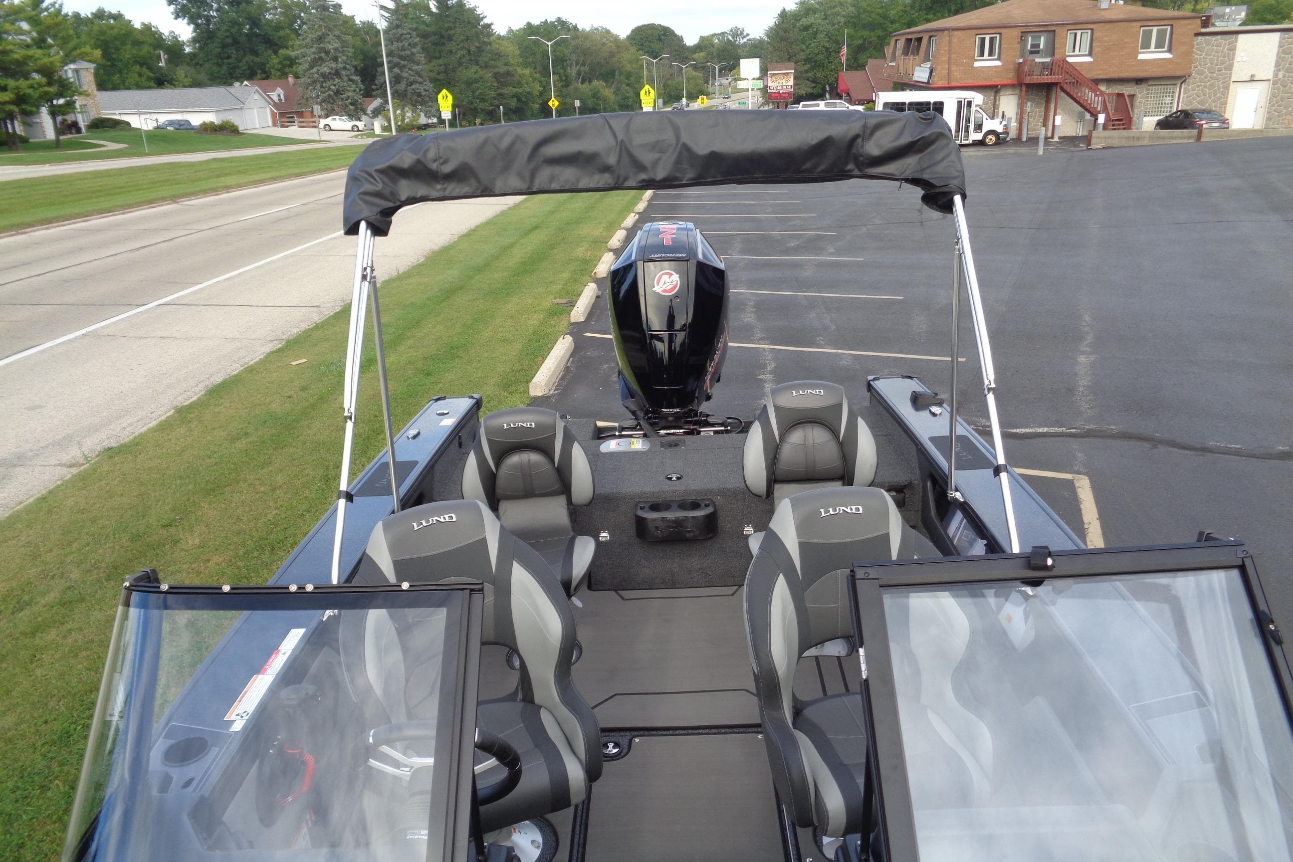 2026 Lund 1875 Crossover XS boat interior with seating and outboard motor, parked on pavement.