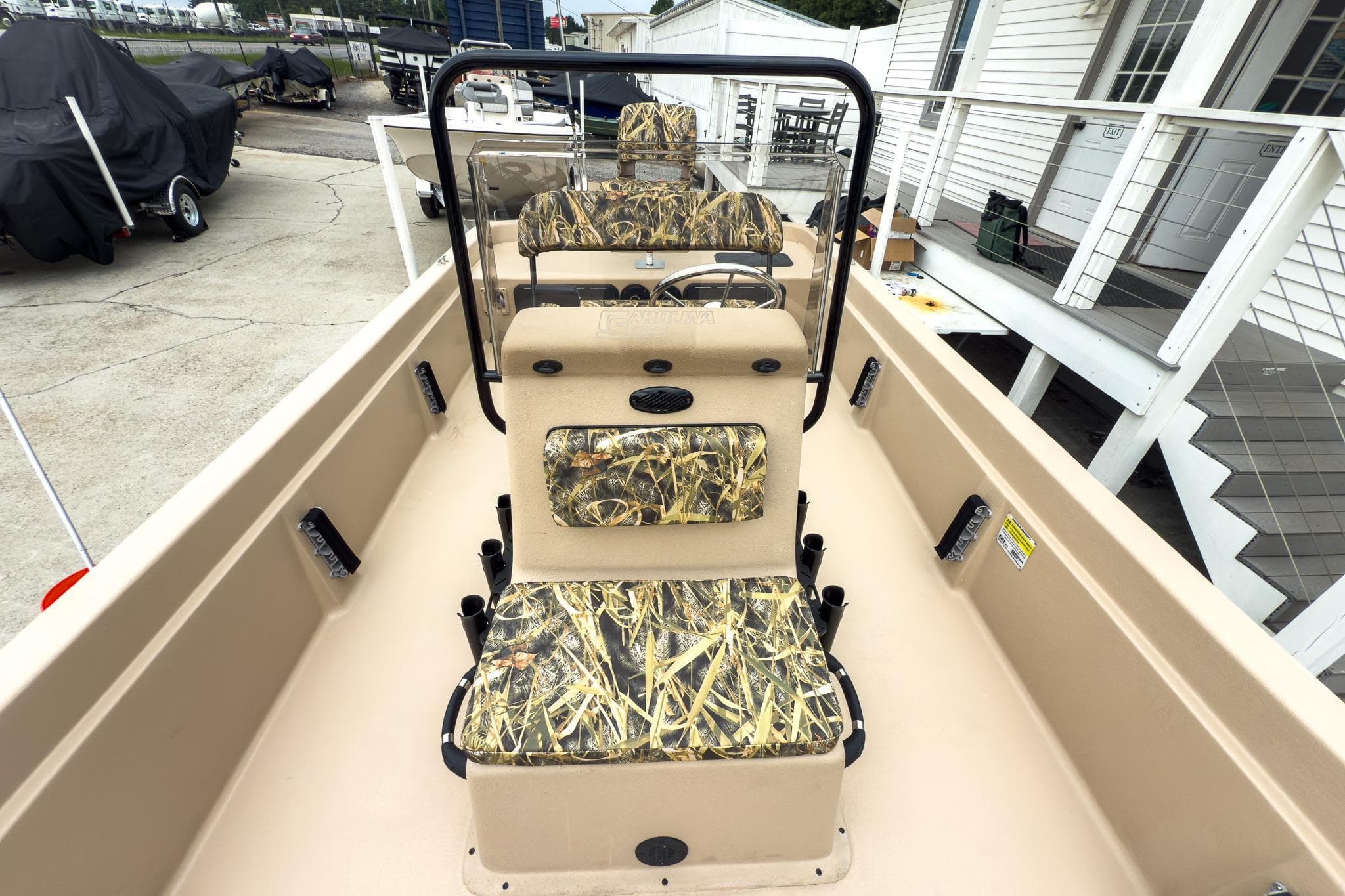 2026 Carolina Skiff E21 DLX CC boat with camouflage seating, docked near a white building.