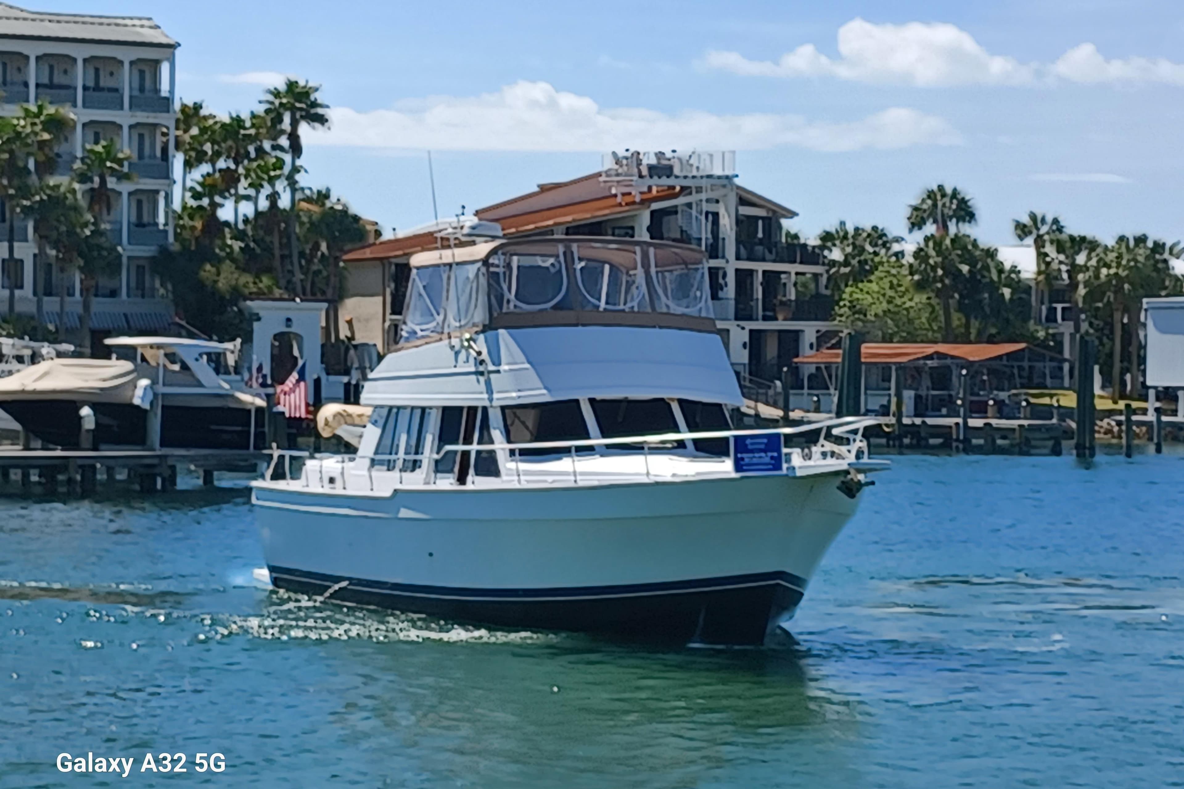 1999 Mainship 43 Trawler Aft Cabin cruising in a marina with palm trees and buildings.
