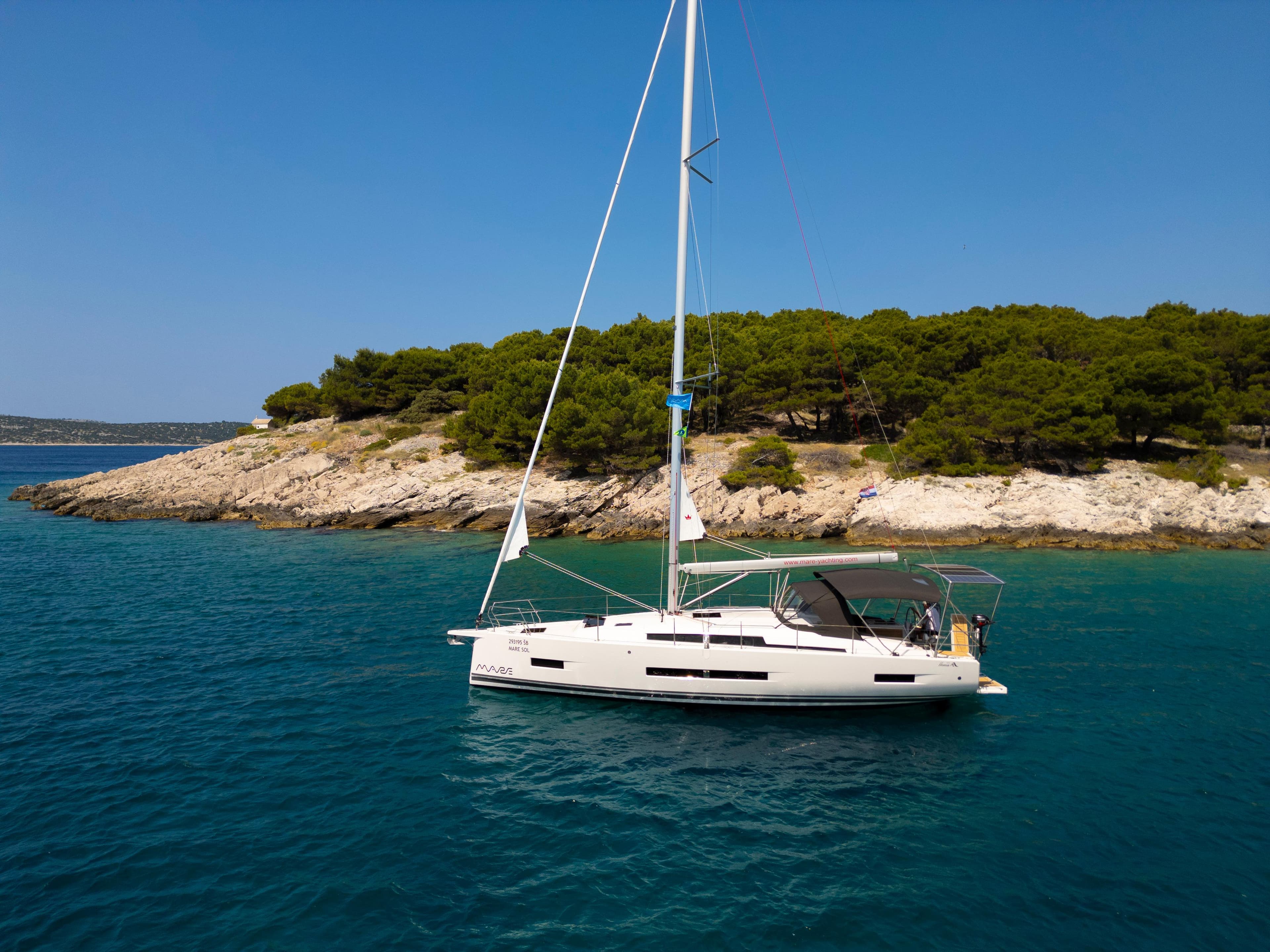 2025 Hanse 410 sailboat anchored near a rocky island with lush greenery.