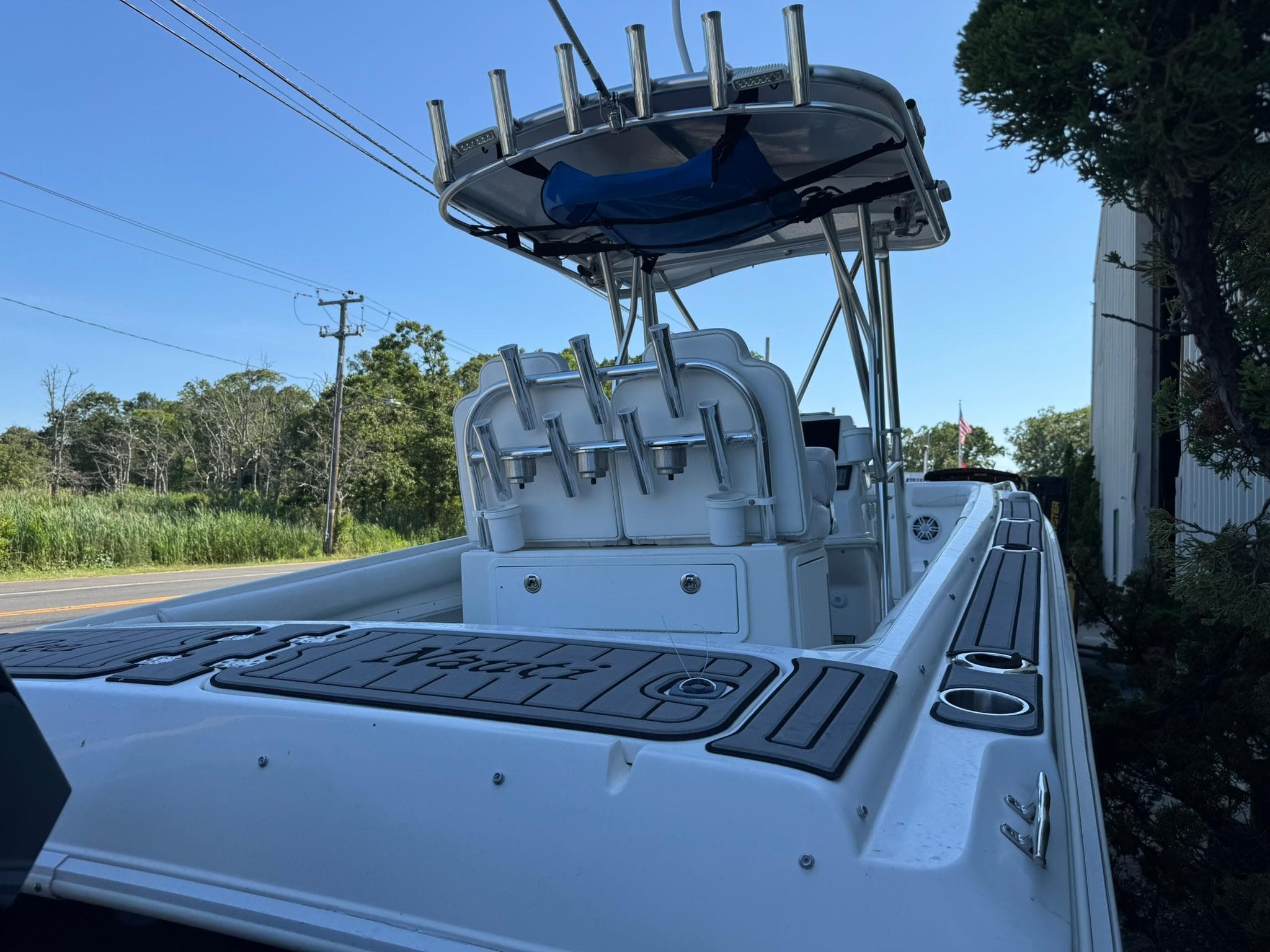 1998 Wellcraft Scarab Sport 302 boat with rod holders and canopy, parked near greenery.