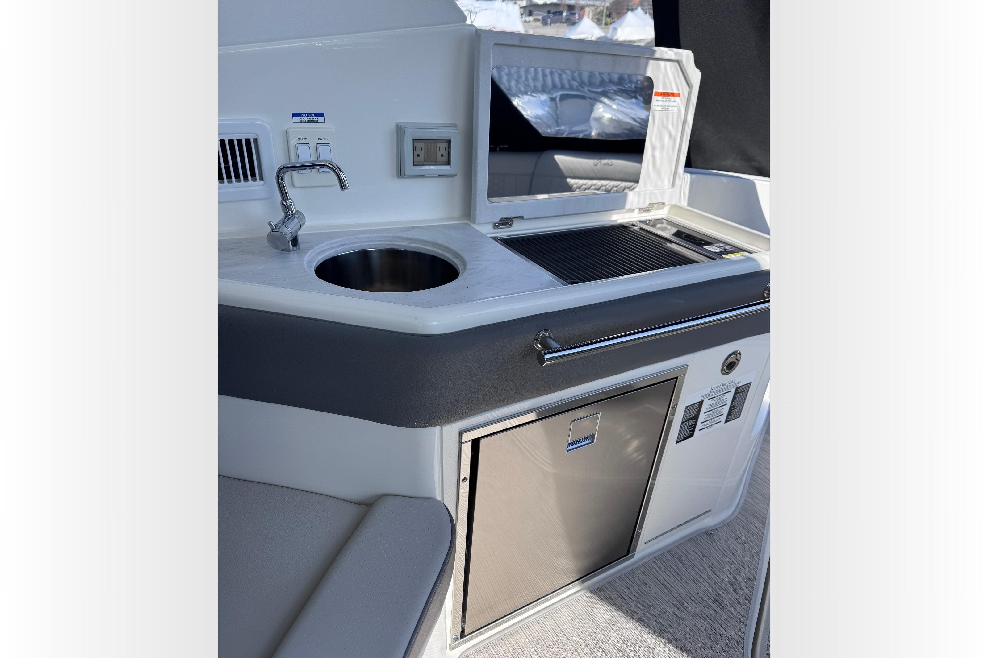 2025 Sea Ray Sundancer 320 boat kitchenette with sink, grill, and stainless steel fridge.