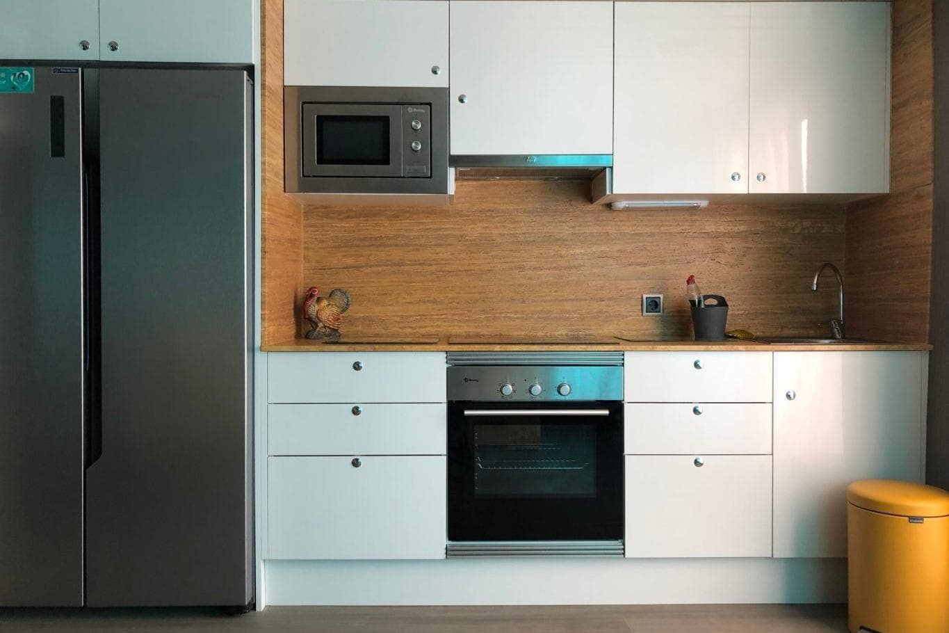 Modern kitchen with stainless steel appliances, white cabinets, and wooden backsplash.