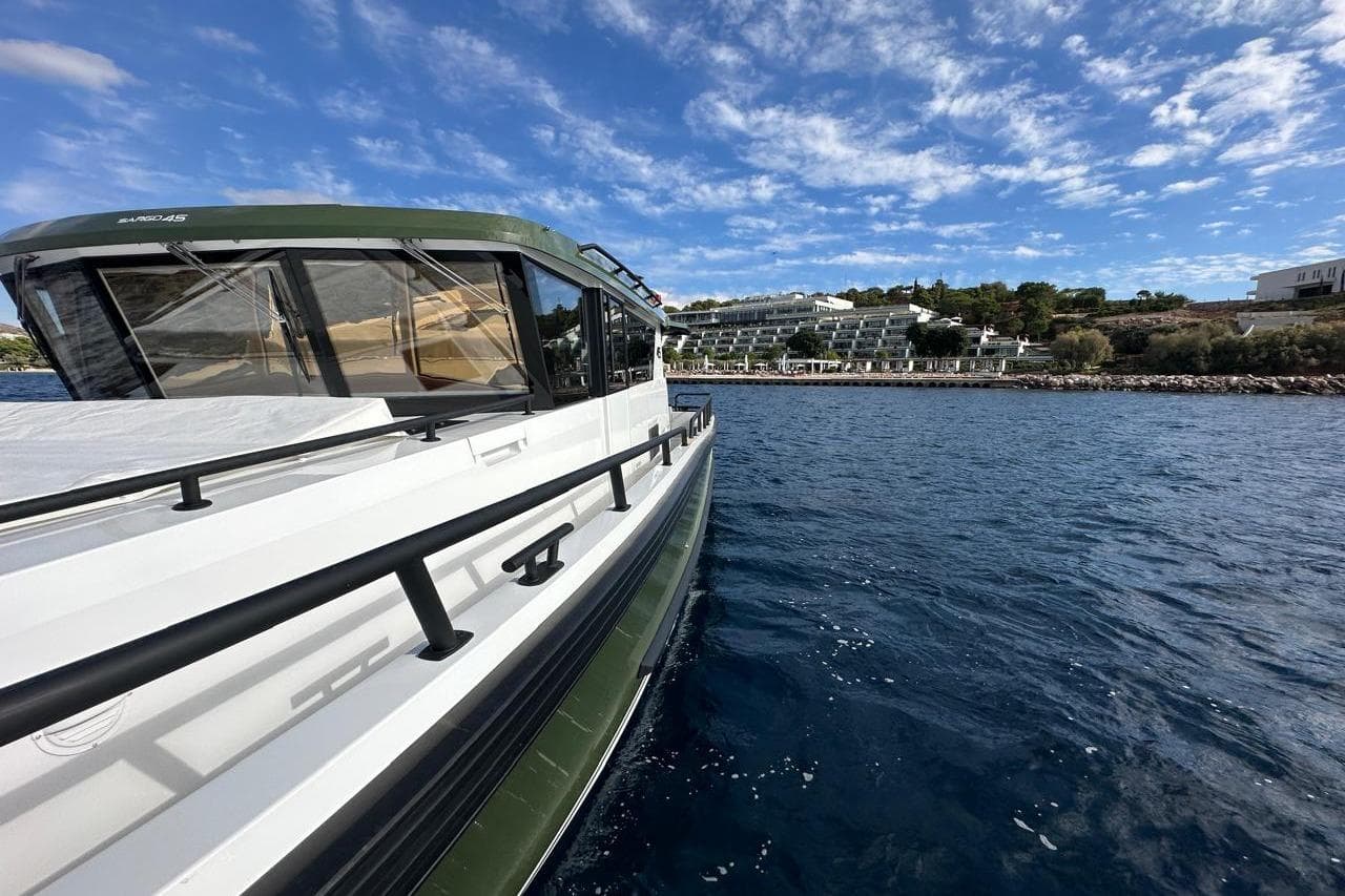 2025 Sargo 45 boat cruising near a scenic coastal resort under a blue sky.