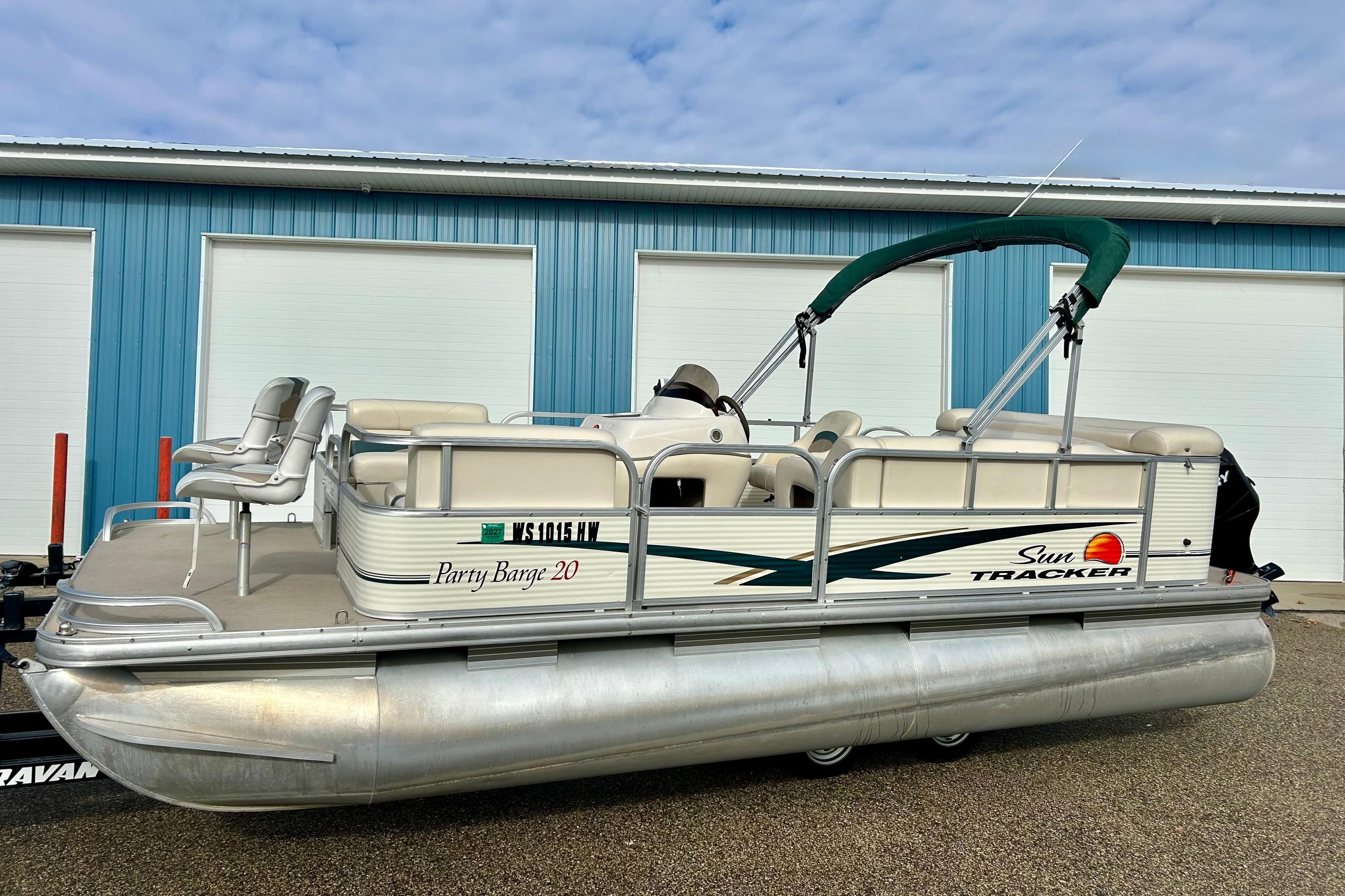 2010 Sun Tracker Party Barge 20 Classic pontoon boat with canopy, parked near blue building.
