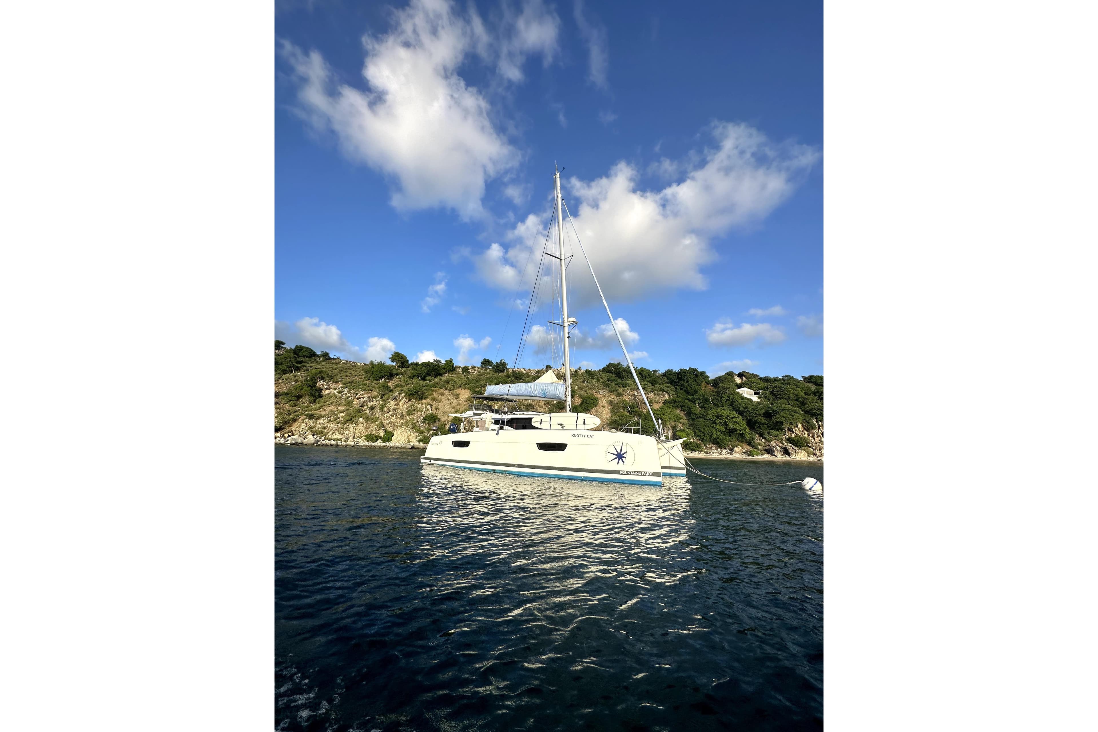 2022 Fountaine Pajot Tanna 47 catamaran anchored near scenic coastline under blue sky.