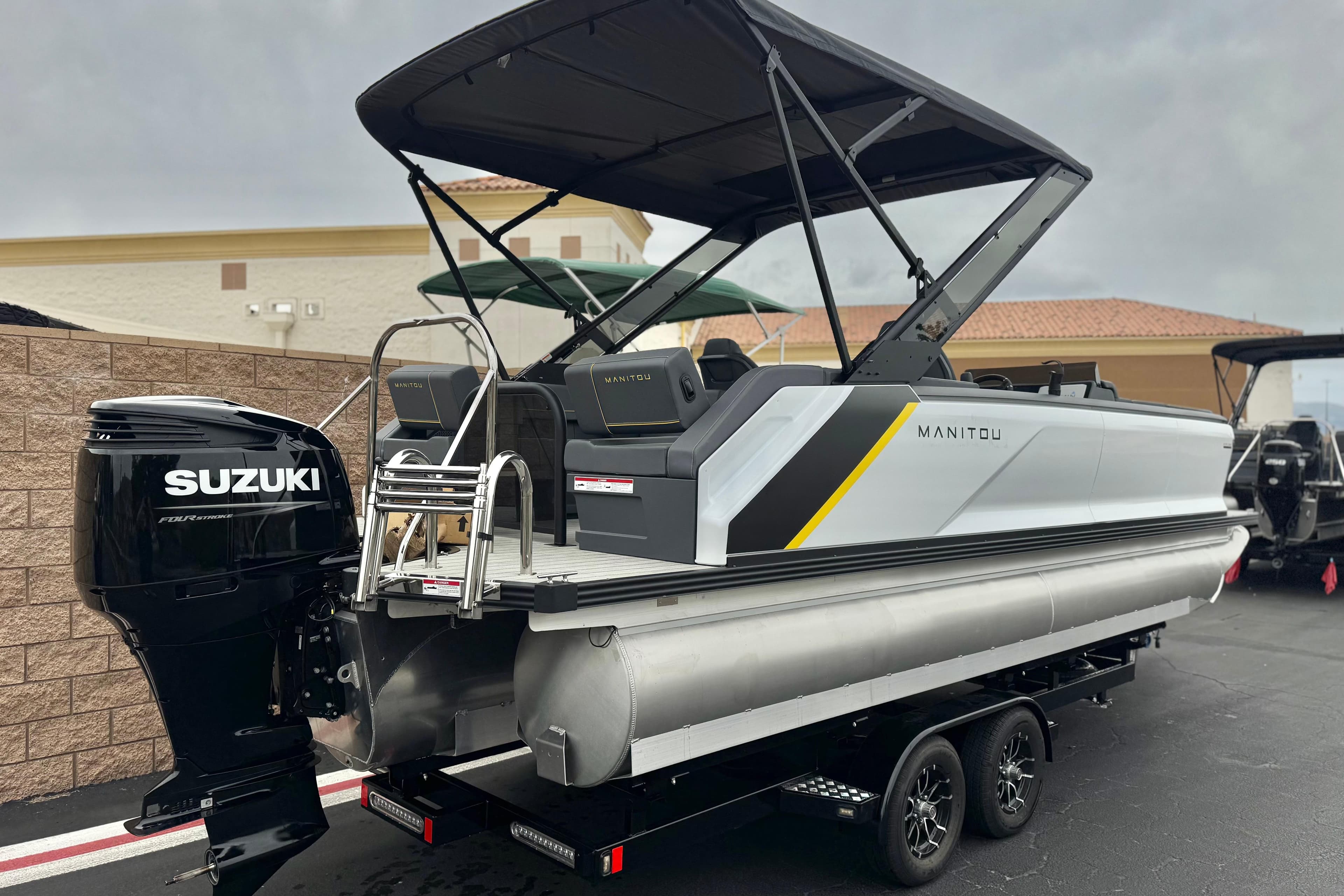 2025 Manitou EXPLORE 24 pontoon boat with Suzuki outboard motor, parked on trailer.