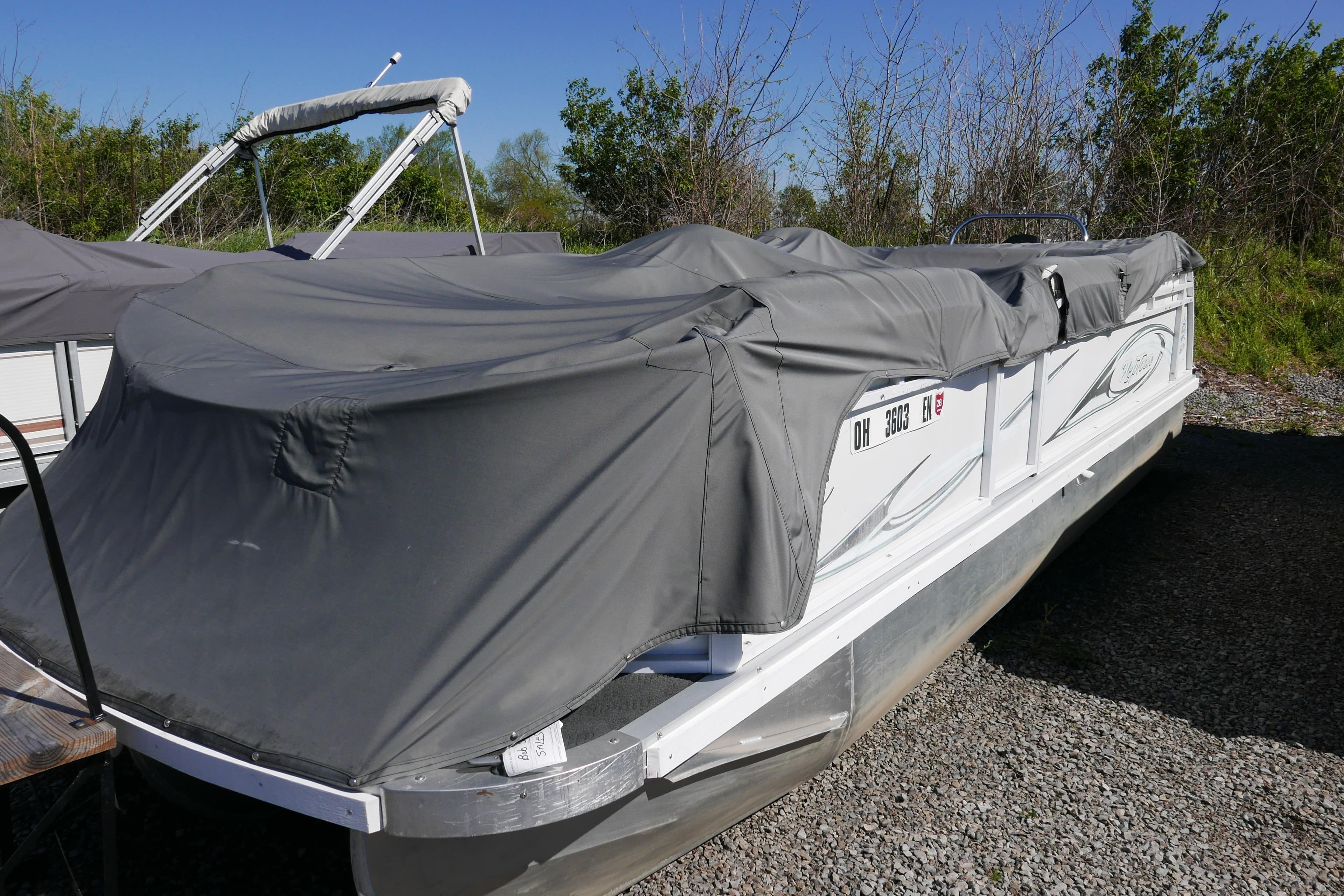 2010 JC Neptoon 21TT pontoon boat covered with a gray tarp, parked outdoors.