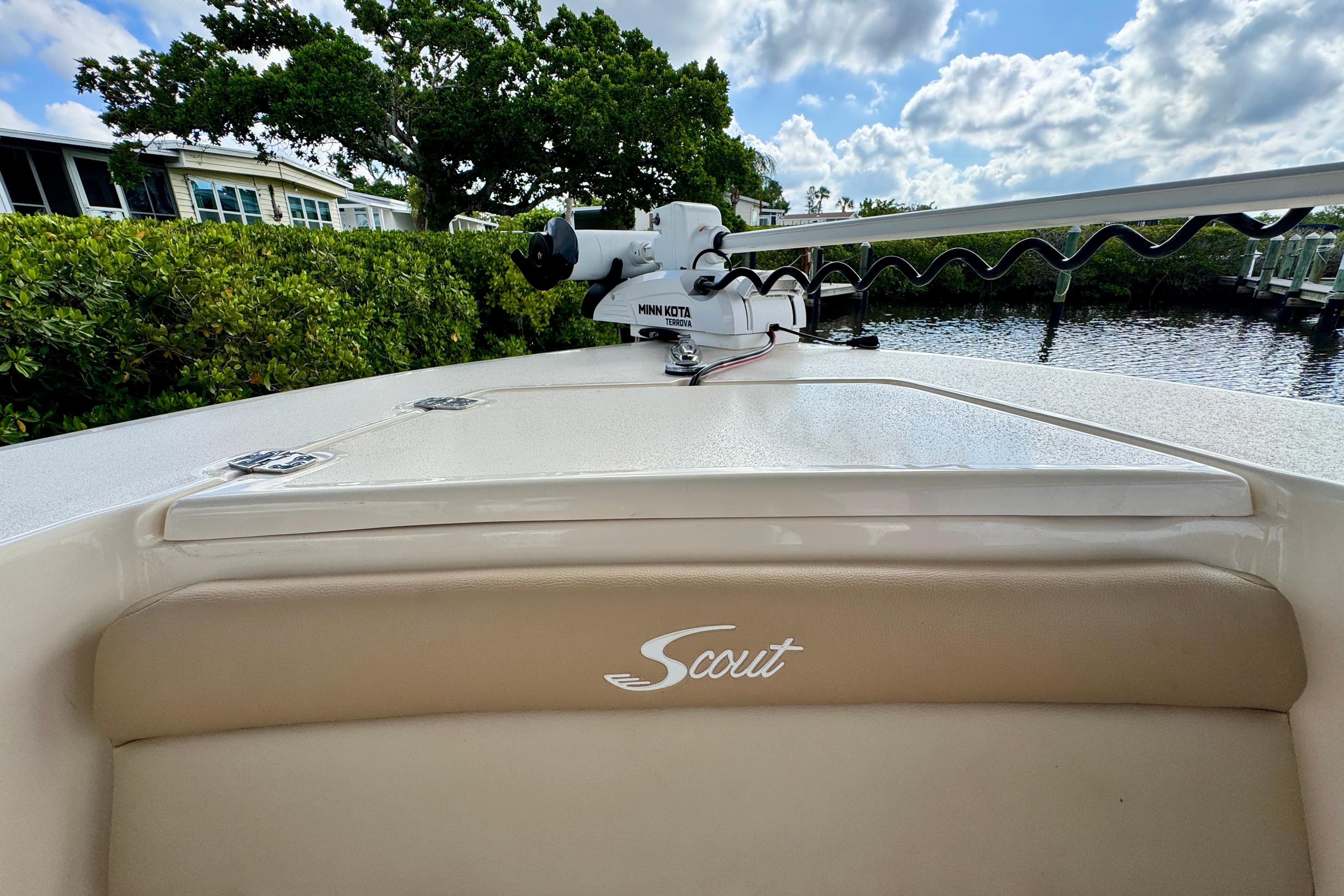 2024 Scout 195 Sportfish boat with Minn Kota motor, docked near lush greenery.