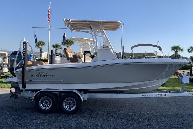 2026 Pioneer ISLANDER 202 boat on trailer, displayed outdoors with flags and palm trees.