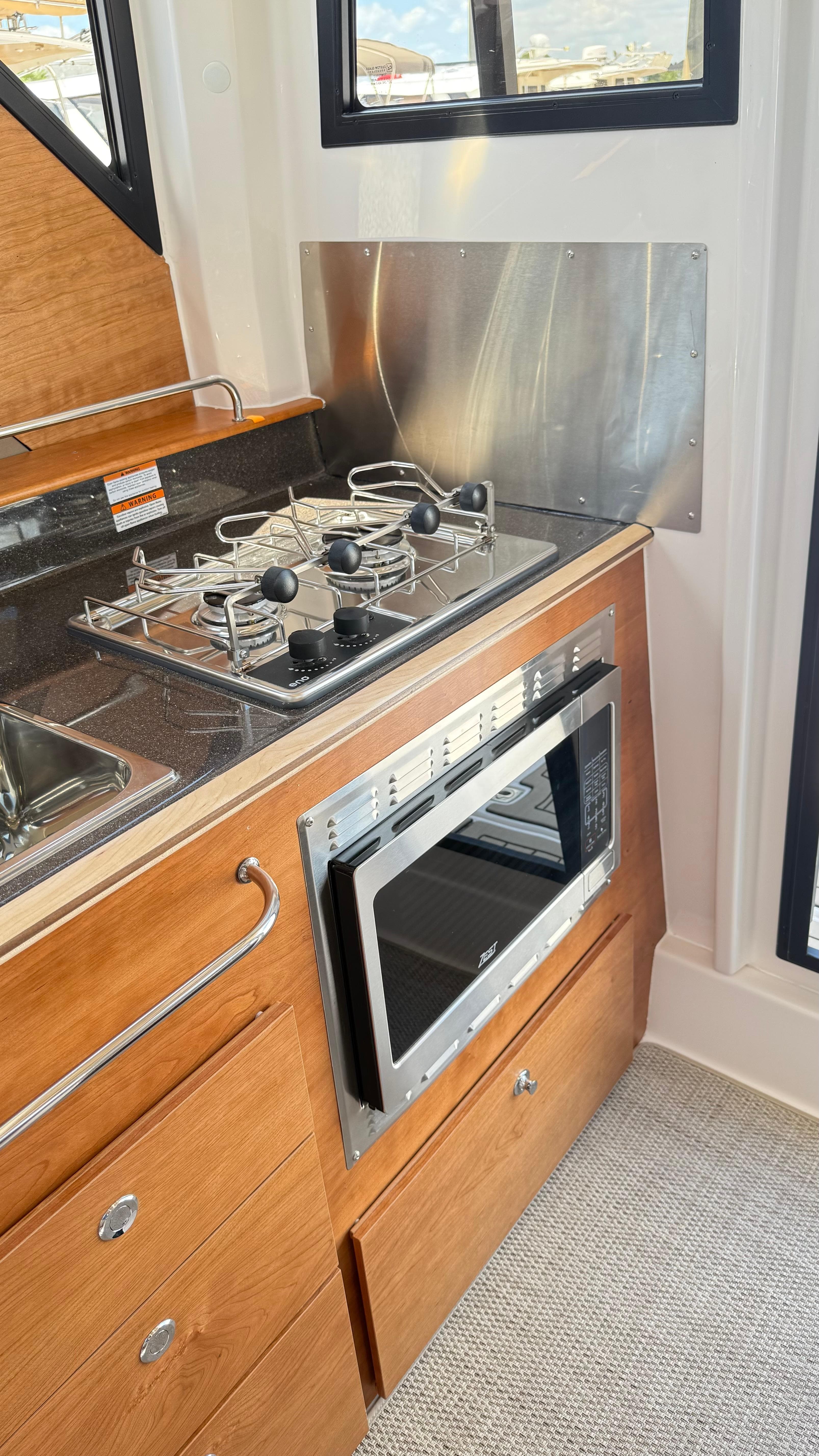 2026 Cutwater C-288 Coupe interior kitchen with stove, microwave, and wooden cabinetry.