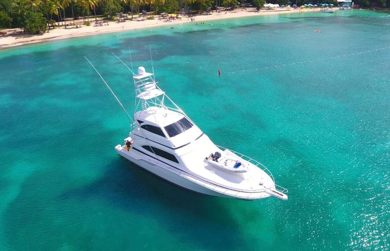Bertram 670 yacht (2004) anchored in clear turquoise waters near a tropical beach.