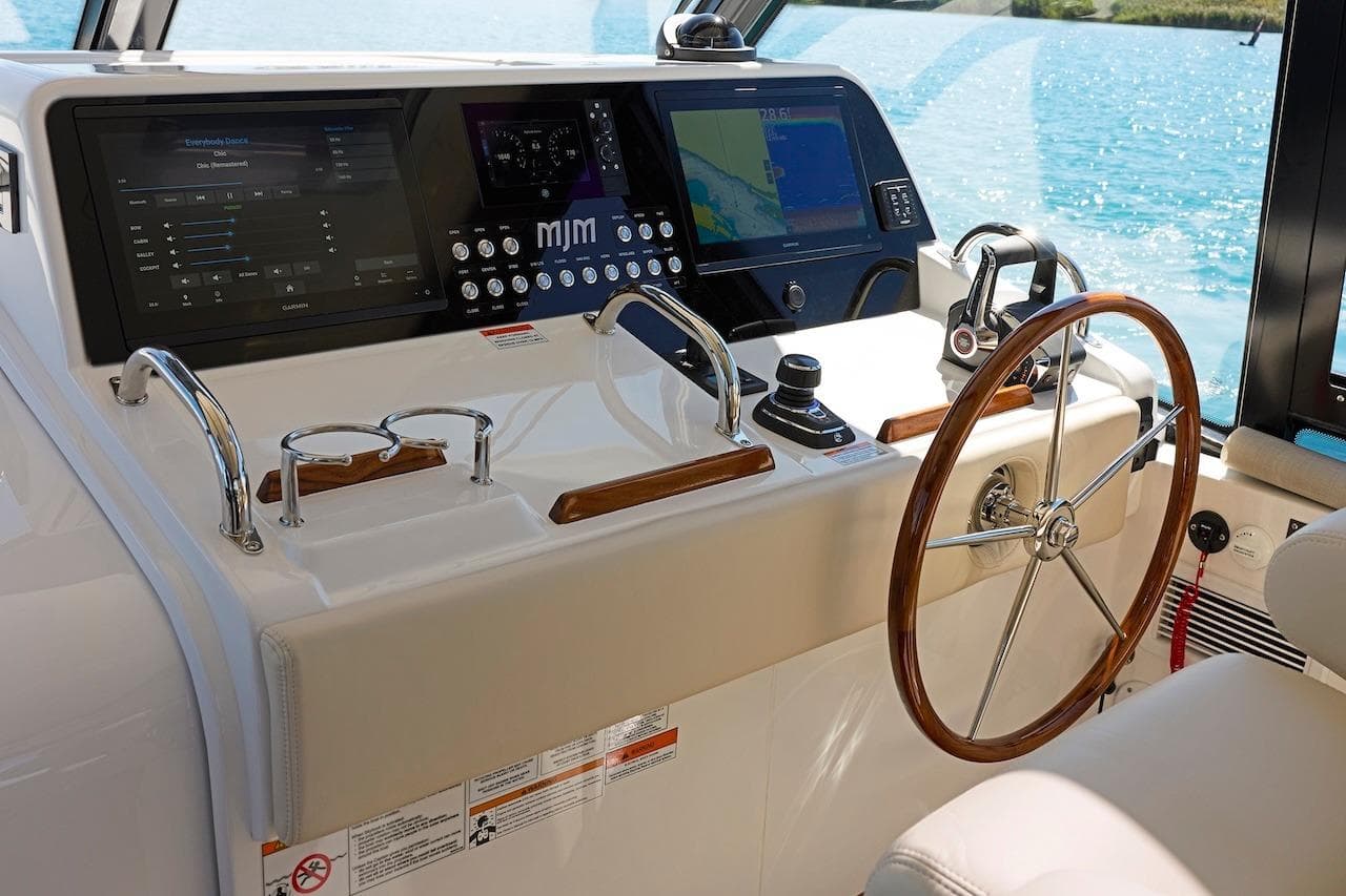 Helm of 2026 MJM 47 X yacht with modern navigation controls and wooden steering wheel.