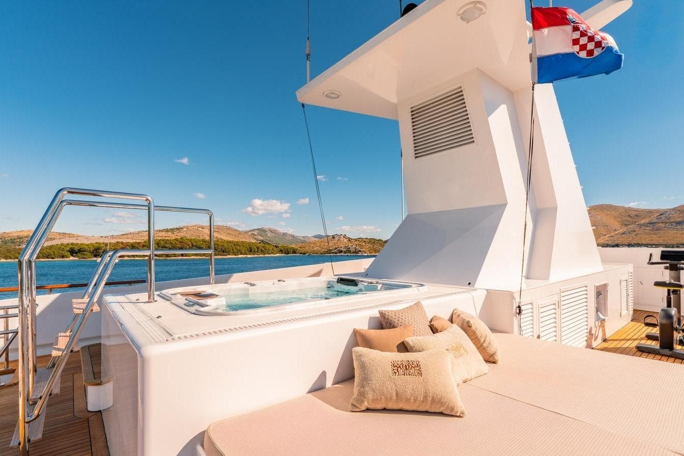 Luxurious 1983 Feadship 55 yacht deck with jacuzzi and sunbathing area, under clear blue skies.