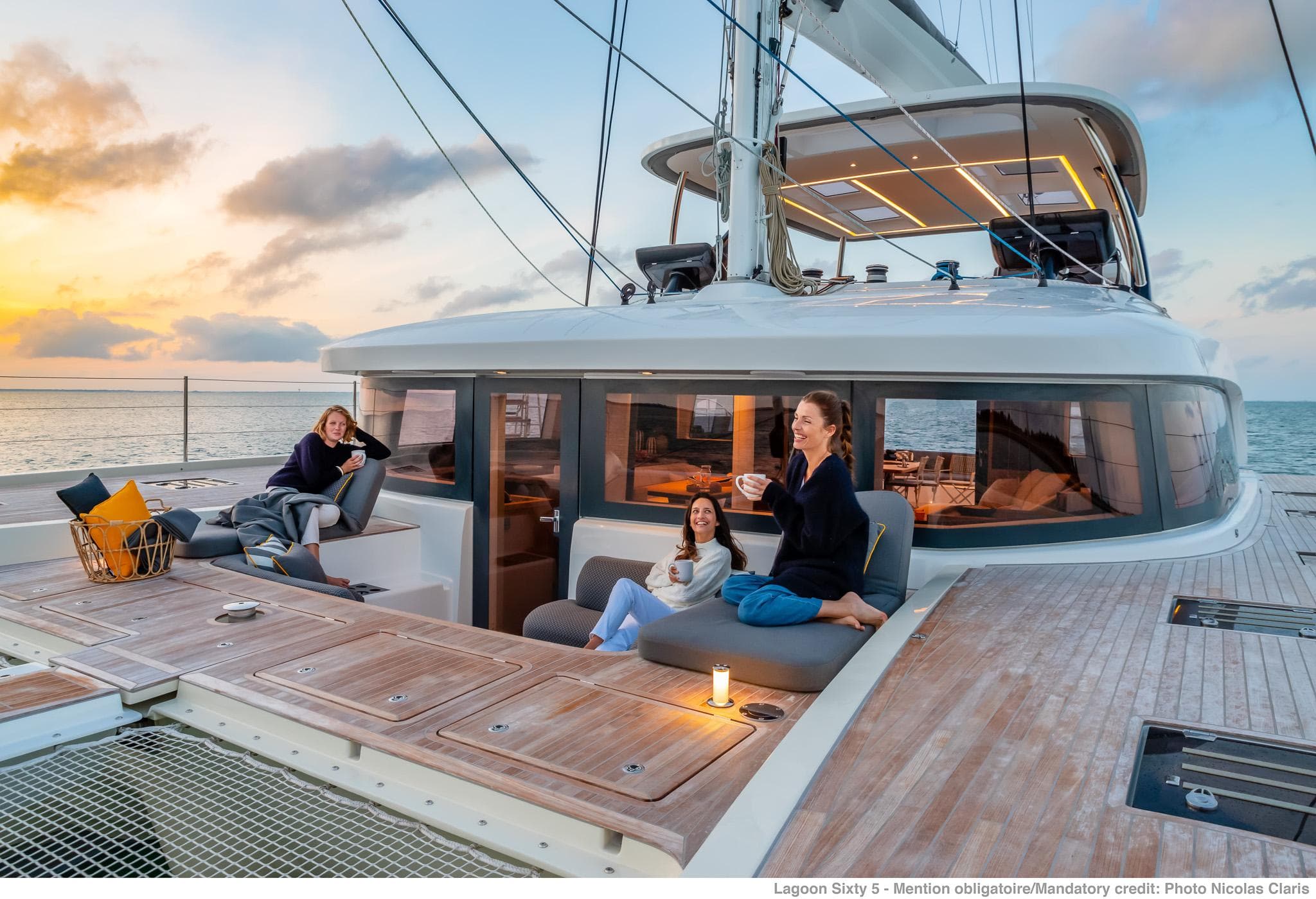 Luxurious 2025 Lagoon SIXTY 5 yacht with people relaxing on deck at sunset.