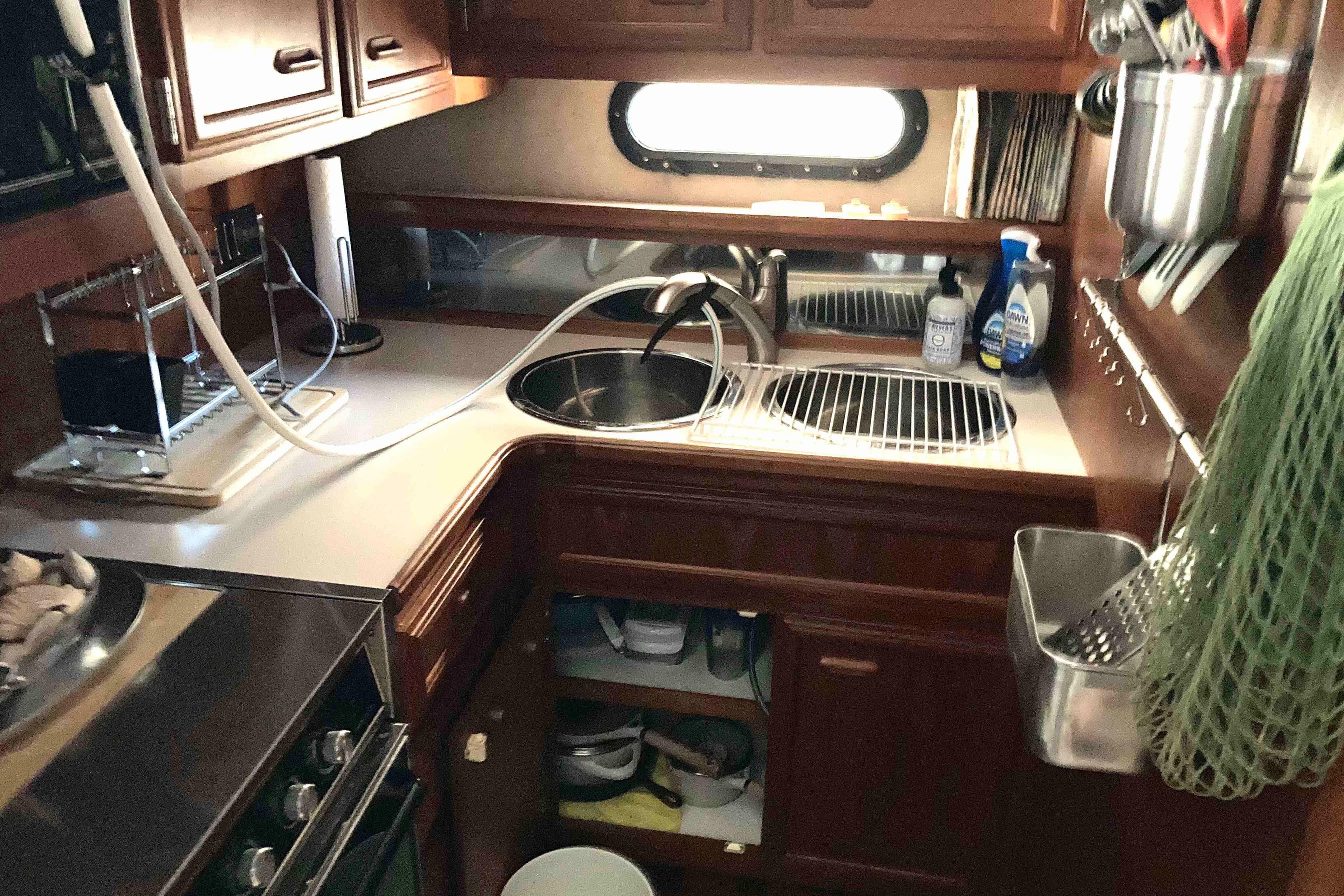 Compact kitchen area in a 1989 Knight & Carver 3807 yacht, featuring wooden cabinetry and modern appliances.