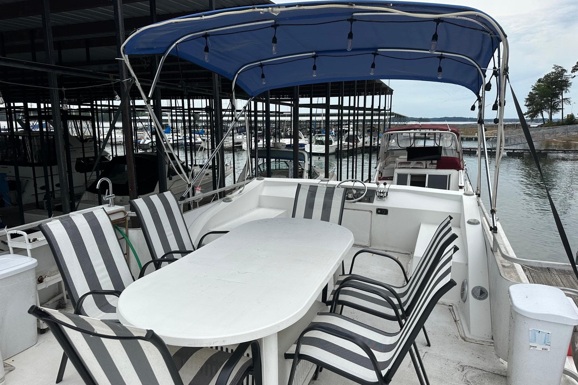 1996 Catamaran Cruisers 12x42 with outdoor seating, docked in a marina under a blue canopy.