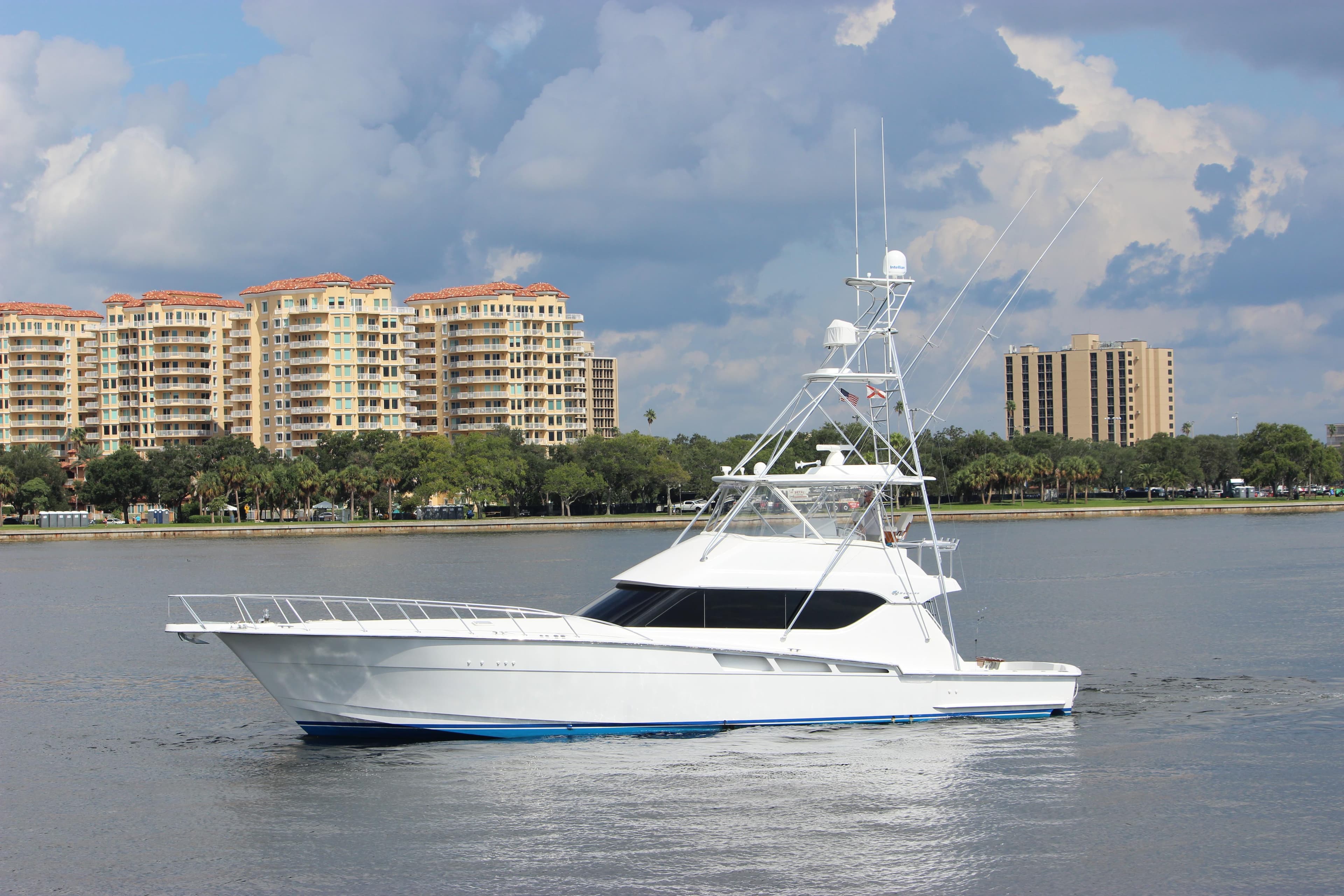 2004 Hatteras 60 Convertible yacht cruising near waterfront buildings under cloudy sky.