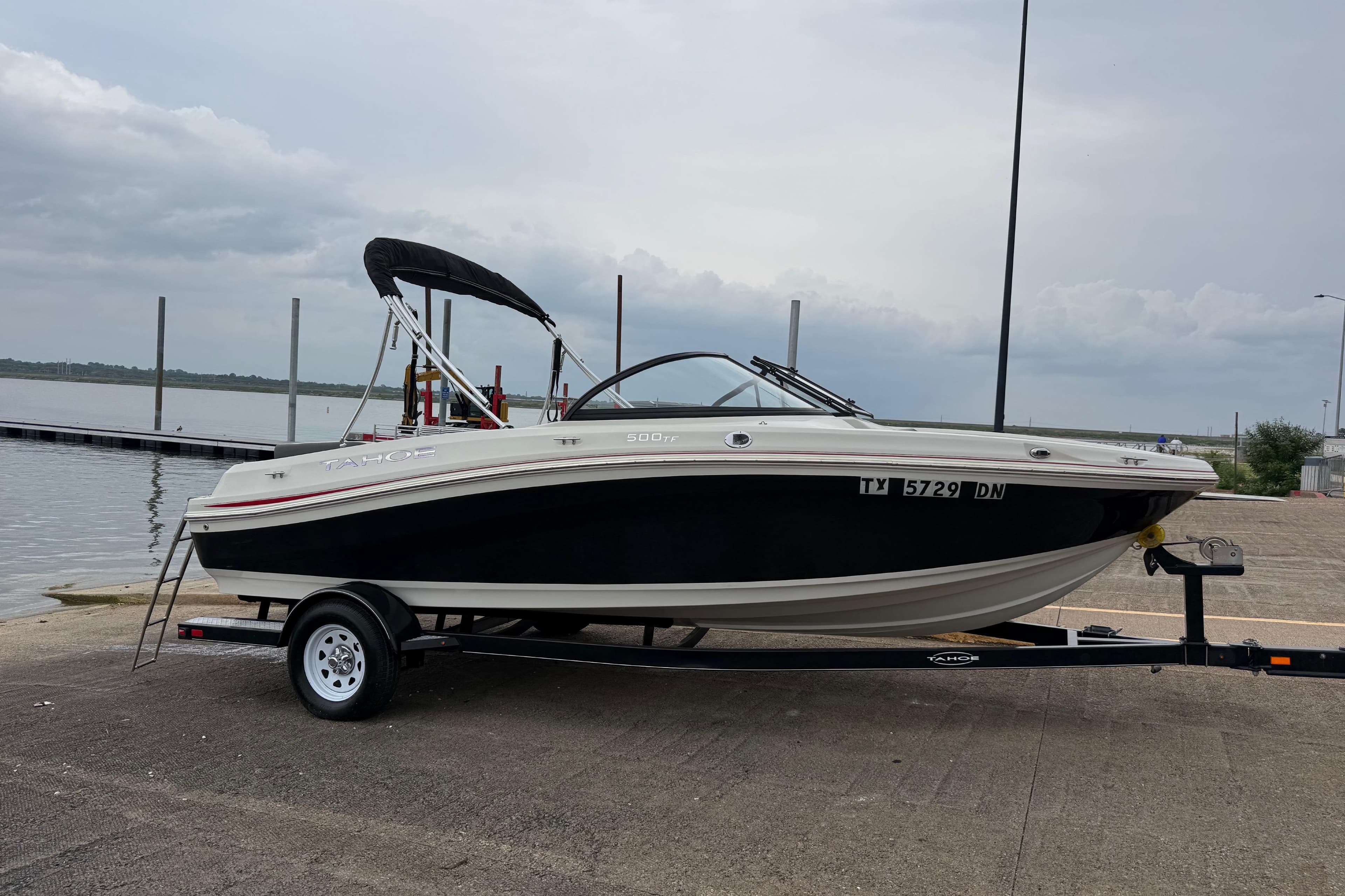 2016 Tahoe 500 TF boat on trailer by a lakeside dock under cloudy skies.
