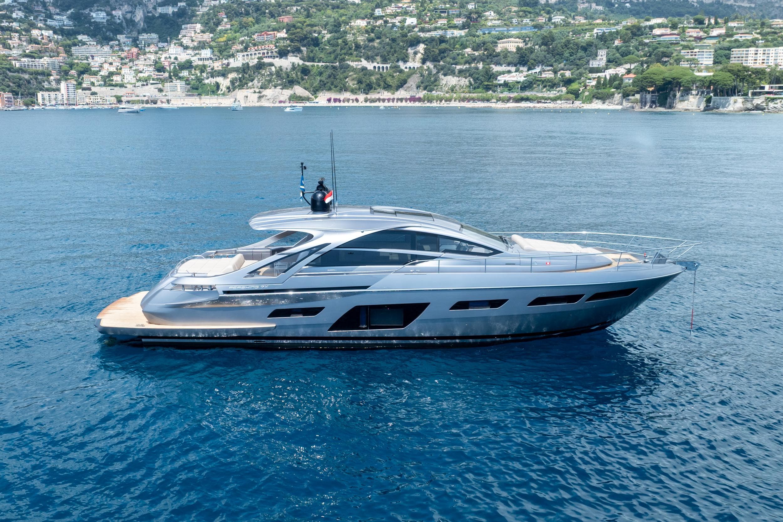 2024 Pershing 7X yacht cruising on clear blue waters near a scenic coastal town.