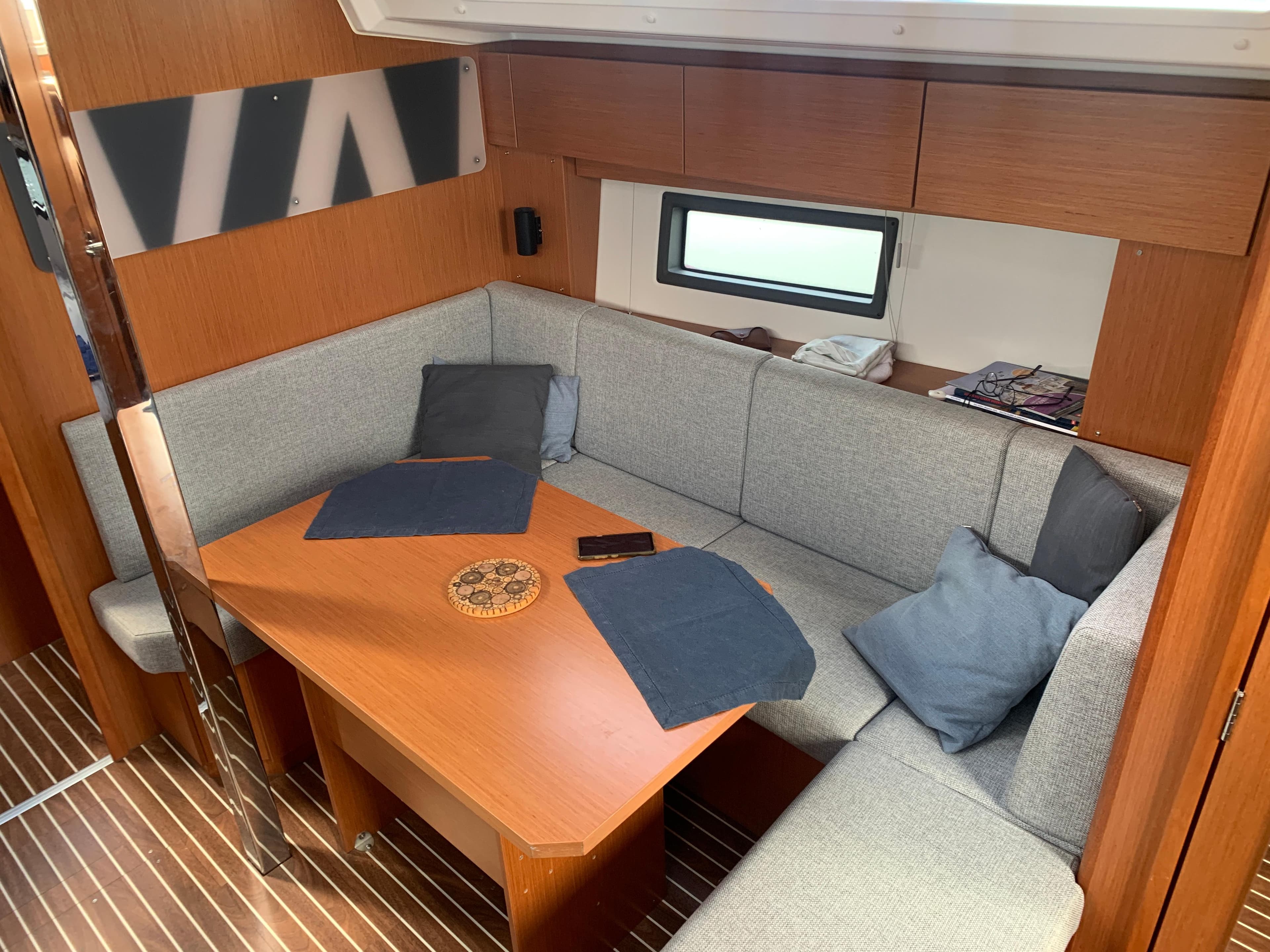 Cozy interior of 2021 Bavaria C38 yacht with wooden table and gray seating.