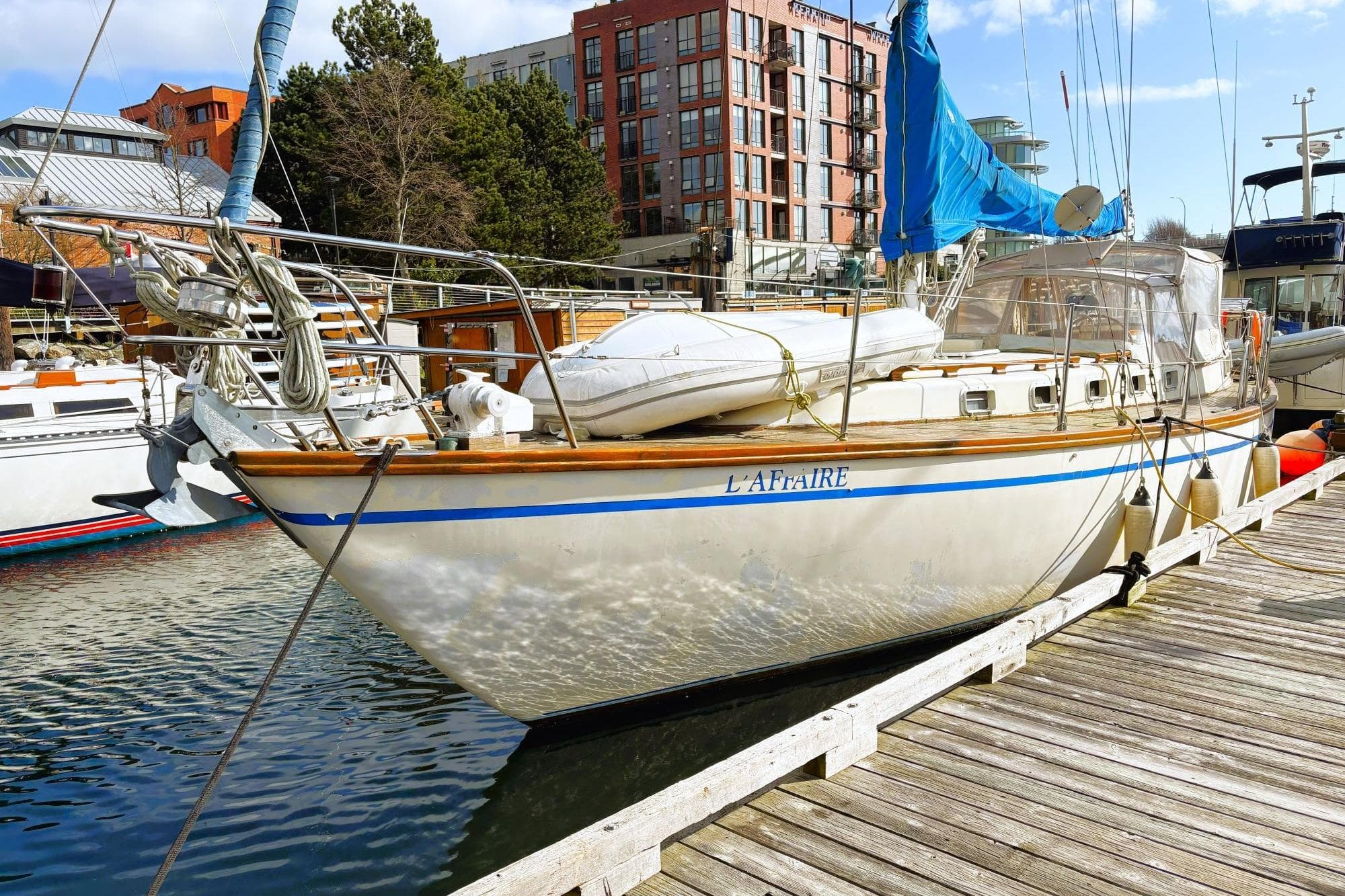 Vintage 1980 Discovery 42 sailboat docked at marina with blue sail and urban backdrop.