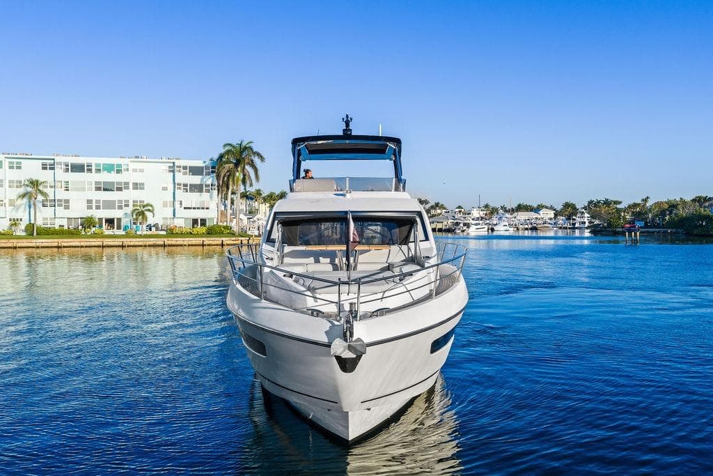 2021 Sunseeker Manhattan 68 yacht on calm water, with buildings and palm trees in the background.