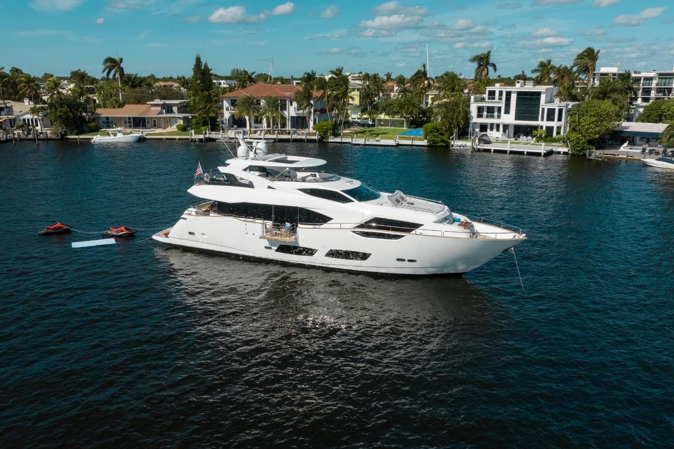 Luxurious 2018 Sunseeker 95 Yacht on serene water, surrounded by elegant waterfront homes.