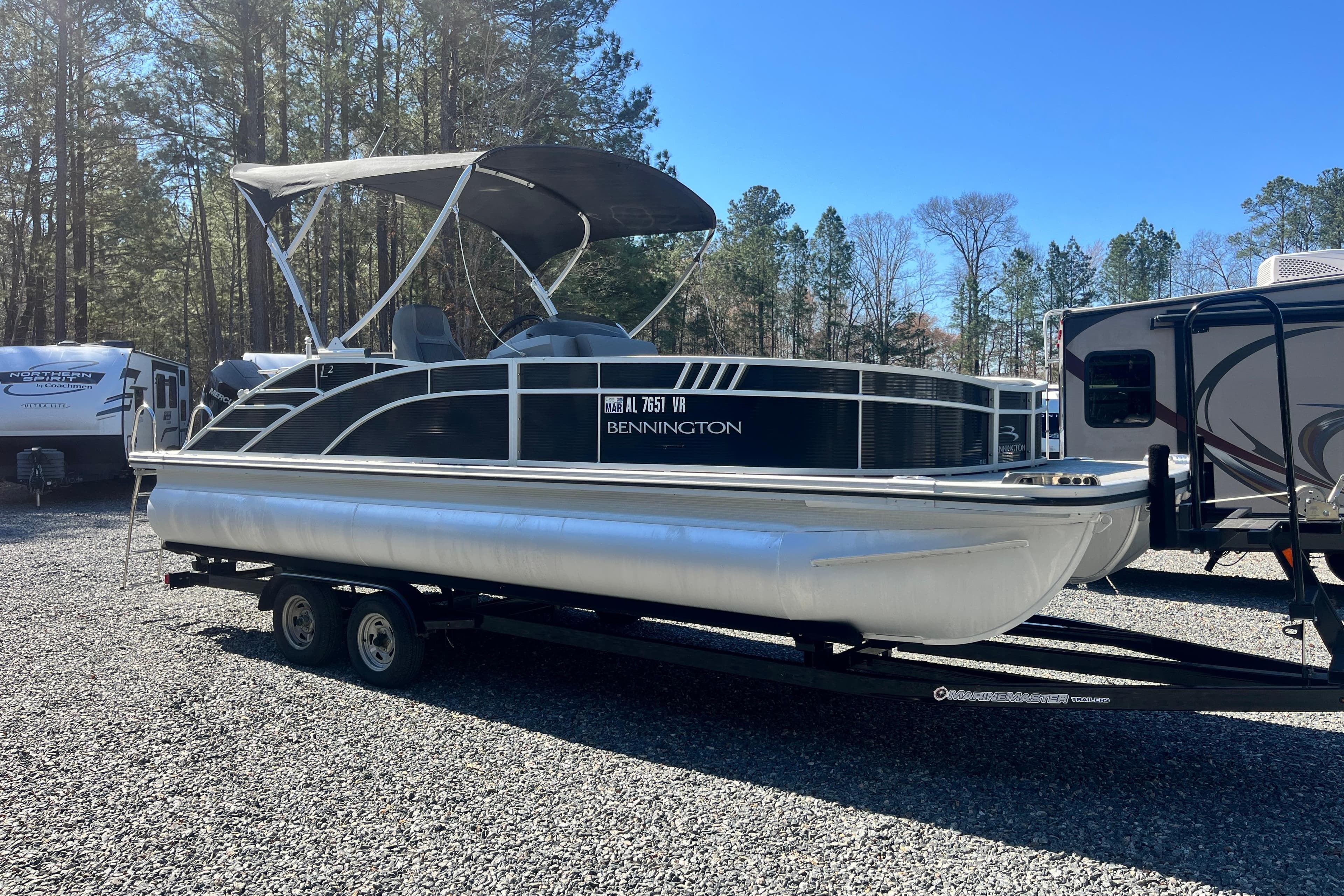 2022 Bennington 23LT pontoon boat on trailer, parked outdoors near RVs and trees.