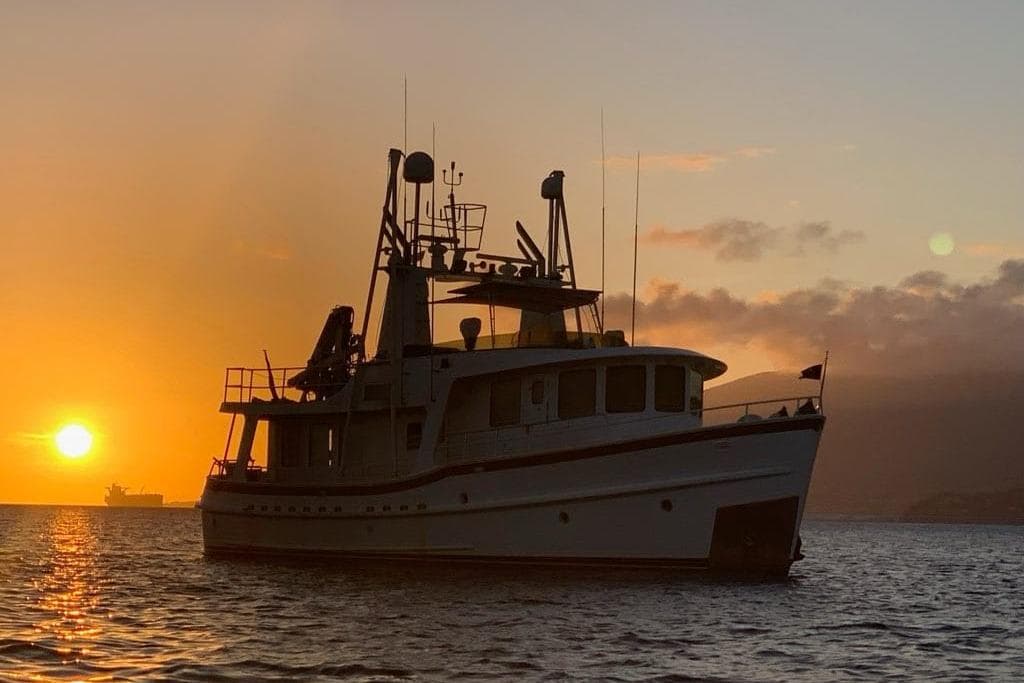 Jones-Goodell 65’ Long Range Trawler, 1992, silhouetted against a vibrant sunset on the water.