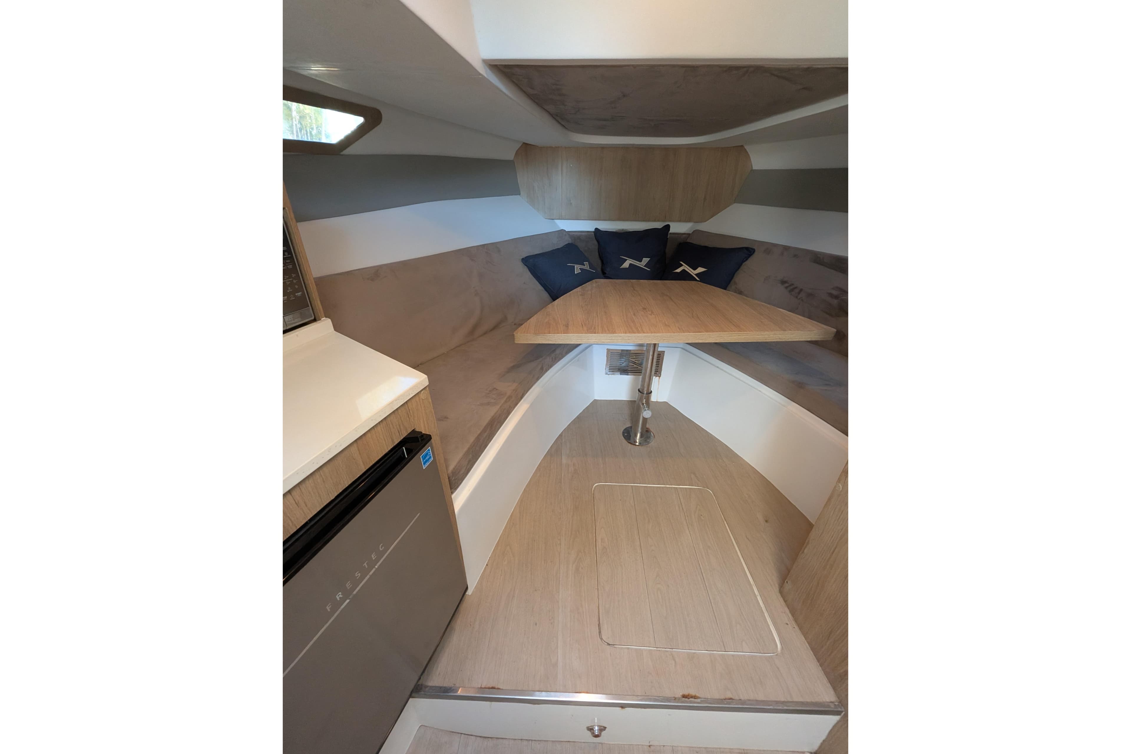 2023 NX Boats 340 Sport Coupe interior with table, cushions, and compact fridge.