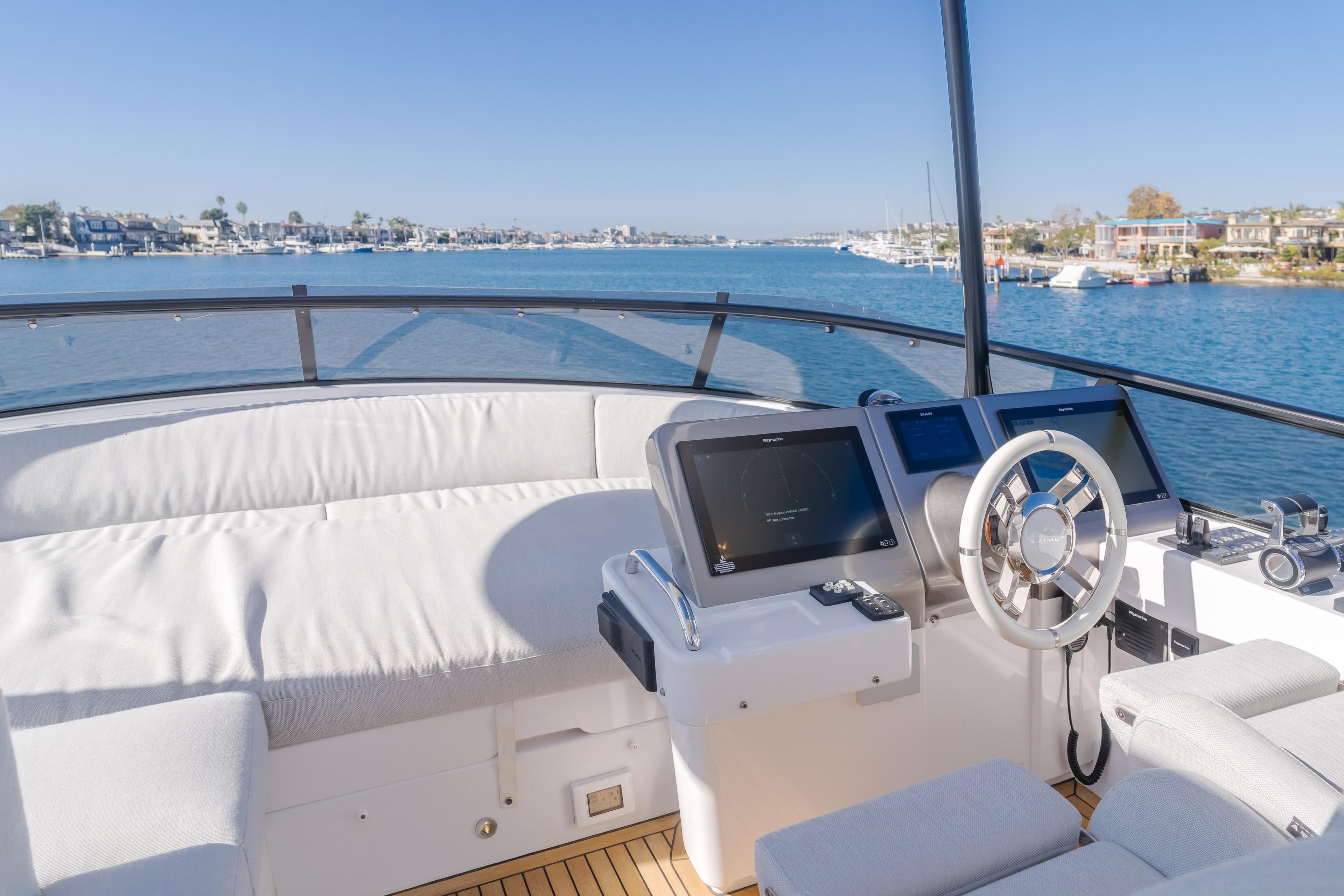 Flybridge of 2023 Azimut Magellano 66 yacht with modern helm and scenic waterfront view.