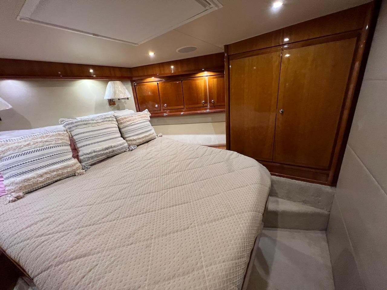 Luxurious bedroom interior of a 2004 Bertram 670 yacht with wooden cabinets and cozy bedding.