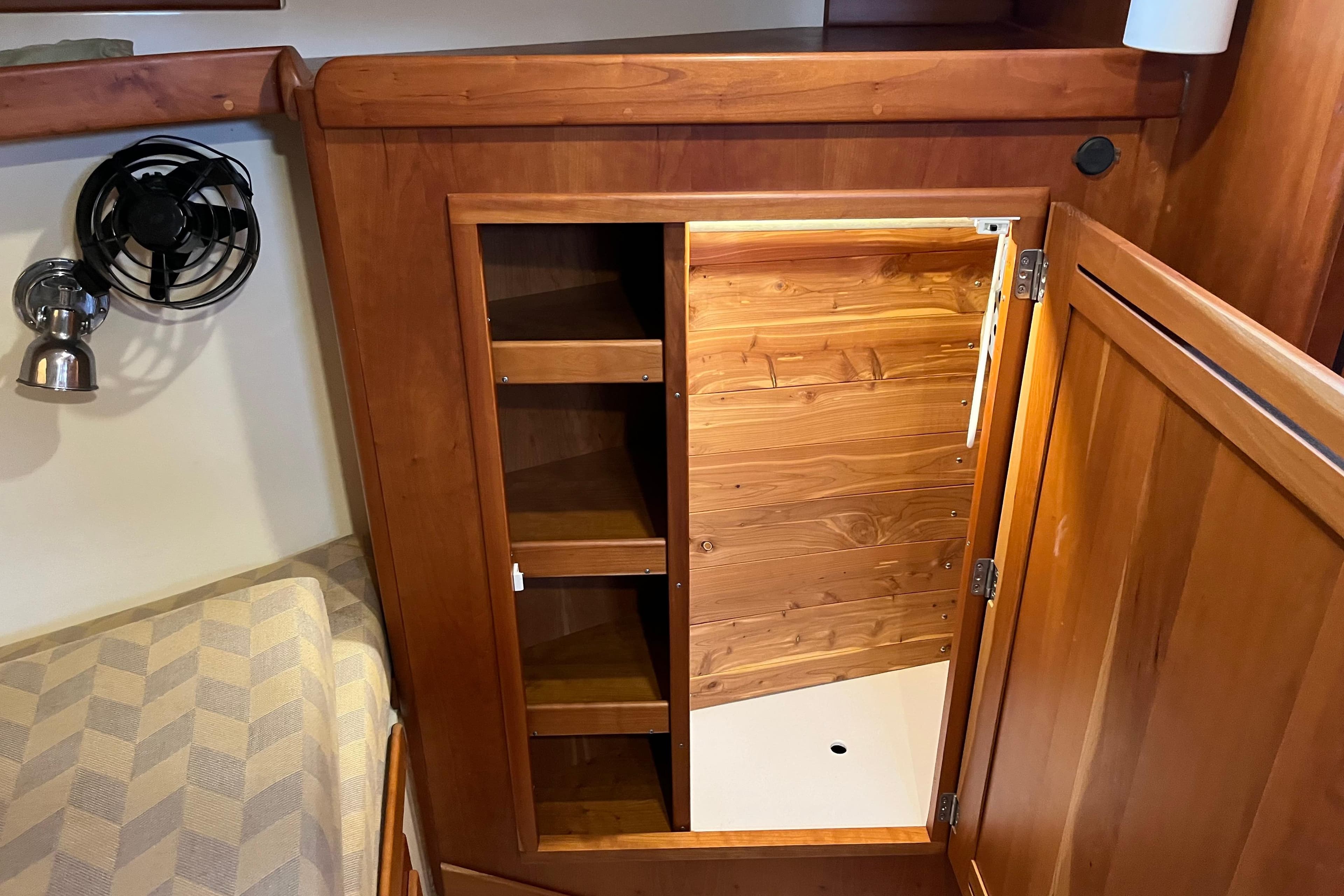 Wooden cabinet interior on a 2004 Tartan 3700 yacht, featuring shelves and a fan.