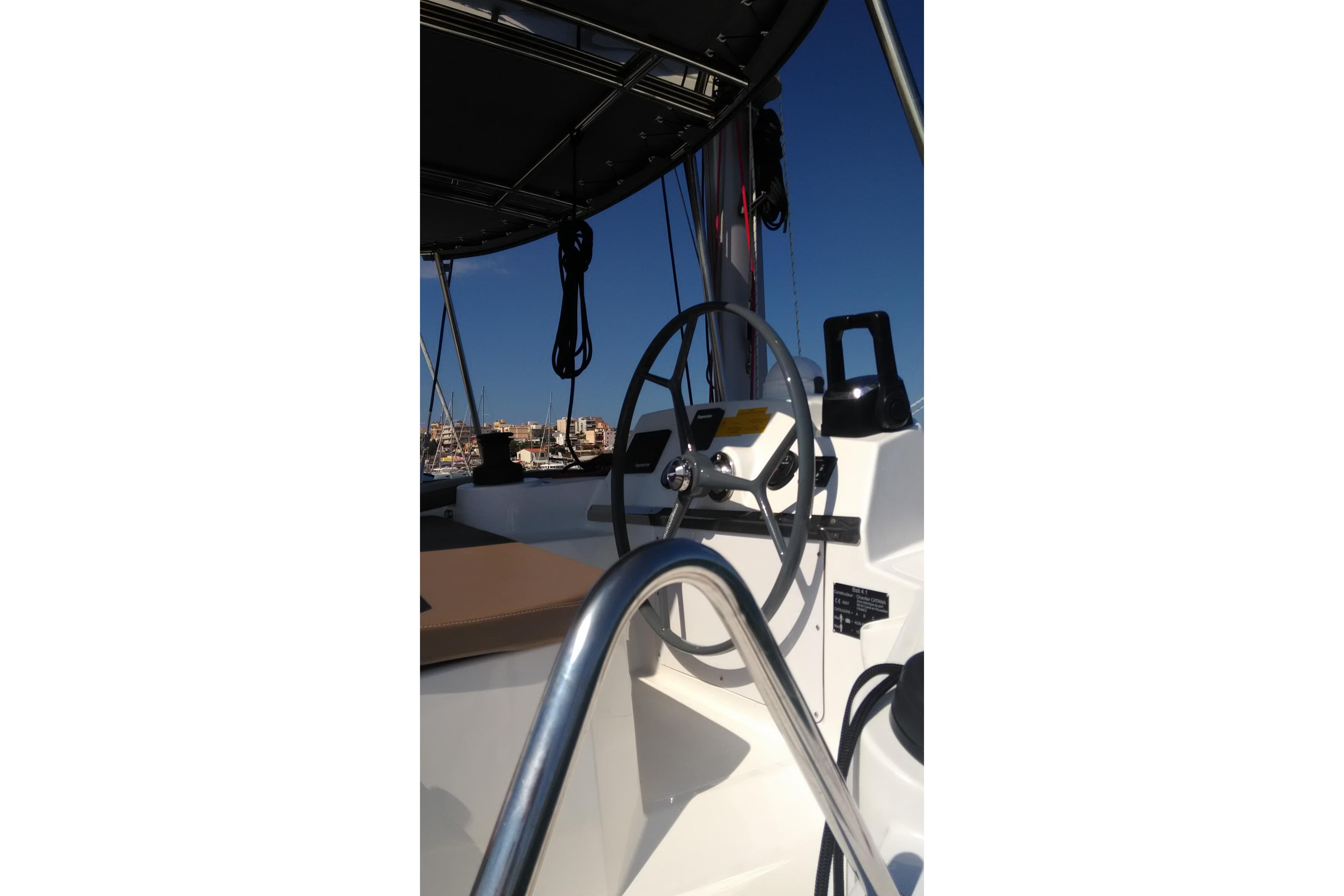 Steering wheel of a 2018 Bali 4.1 catamaran under clear blue sky.