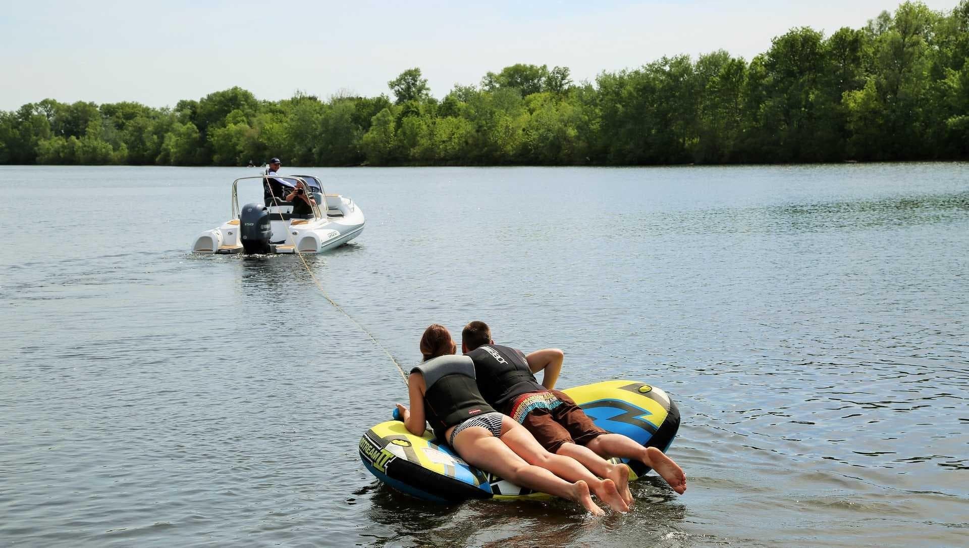 People tubing behind a 2024 Grand Inflatables G580 boat on a lake.