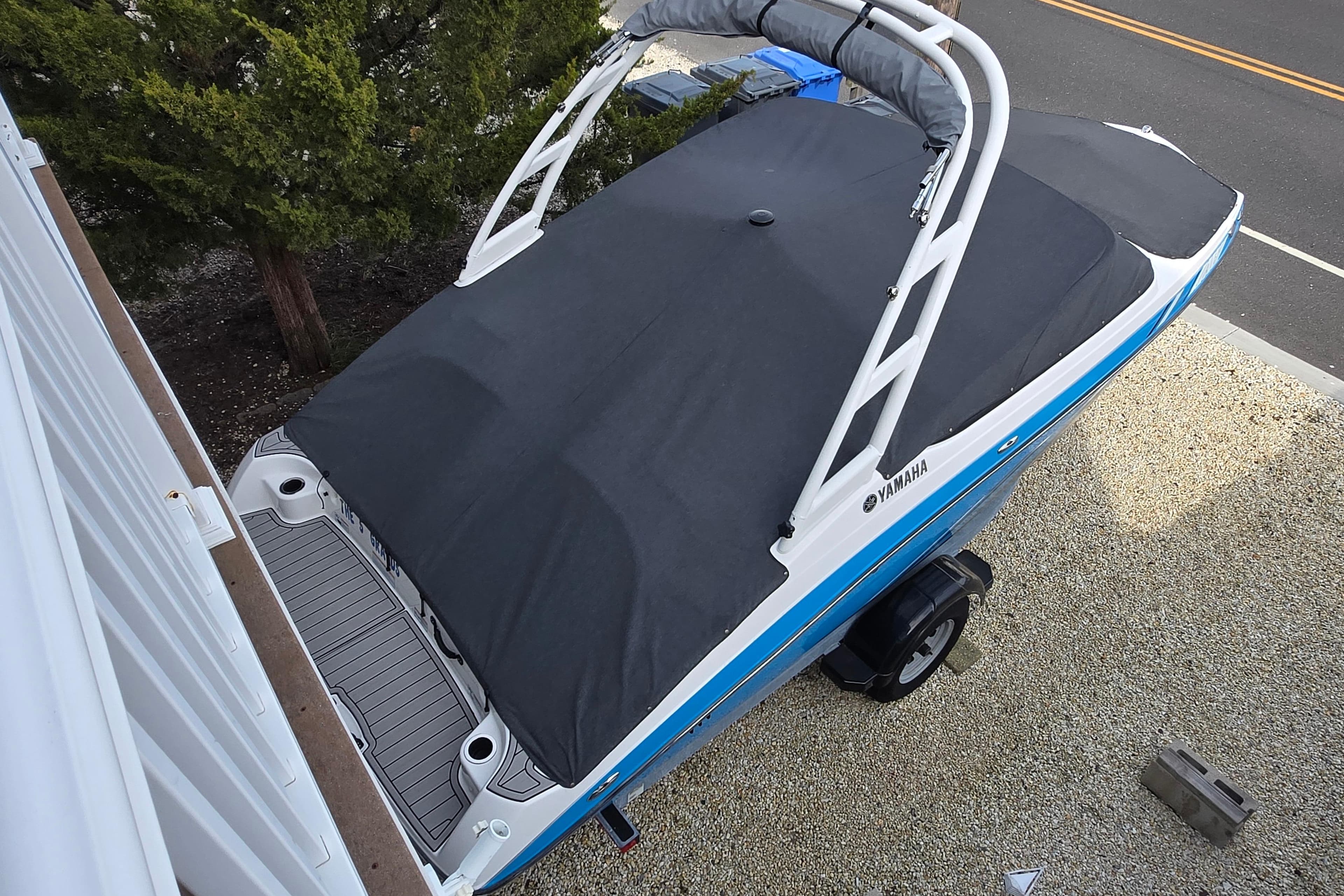 2021 Yamaha Boats AR195 covered, parked on gravel near a road and trees.