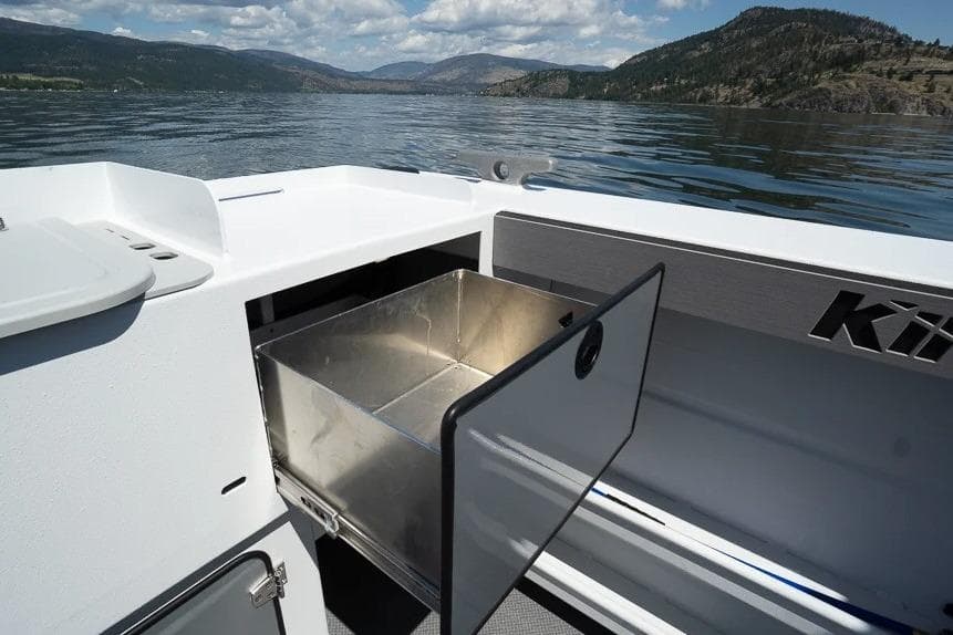 Open storage compartment on 2026 KingFisher 2325 Coastal Express boat, scenic lake view.