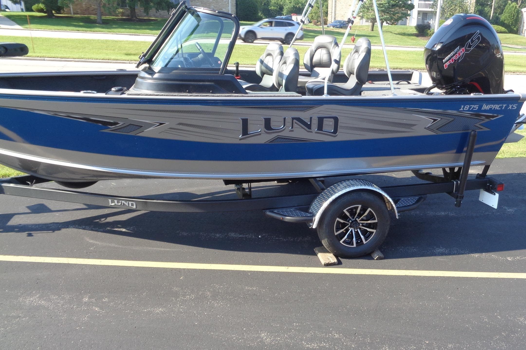 2026 Lund 1875 Impact XS Sport boat on trailer, blue and silver design, parked outdoors.