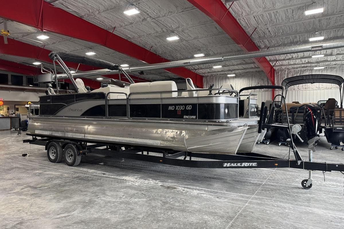 2016 Manitou 24 Aurora LE Angler pontoon boat on trailer in indoor showroom.