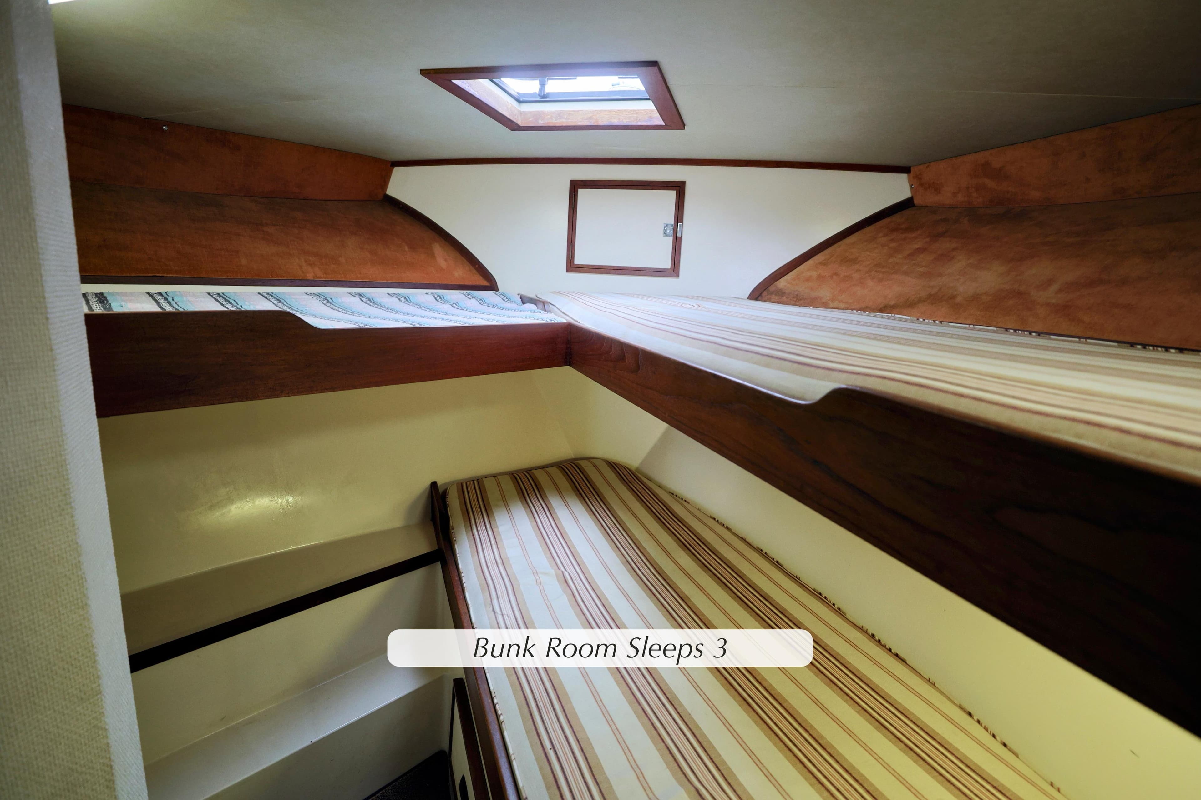 Bunk room in 1980 Pacifica 41 Sportfisher, featuring three beds and wooden accents.