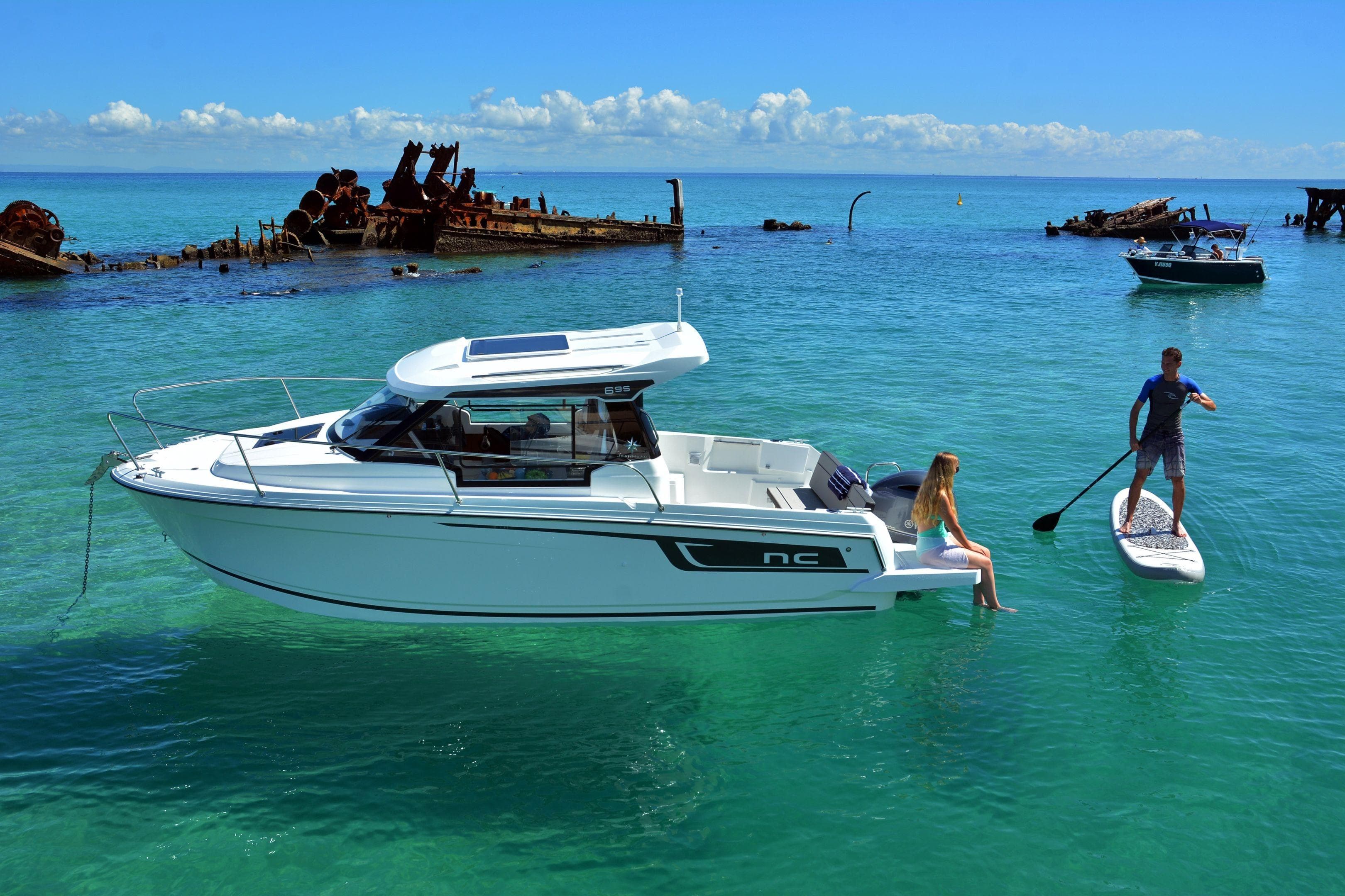 2026 Jeanneau NC 695 boat with people enjoying paddleboarding in clear turquoise waters.