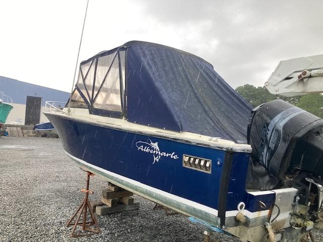1982 Albemarle 24 boat with blue cover, parked on gravel under cloudy sky.