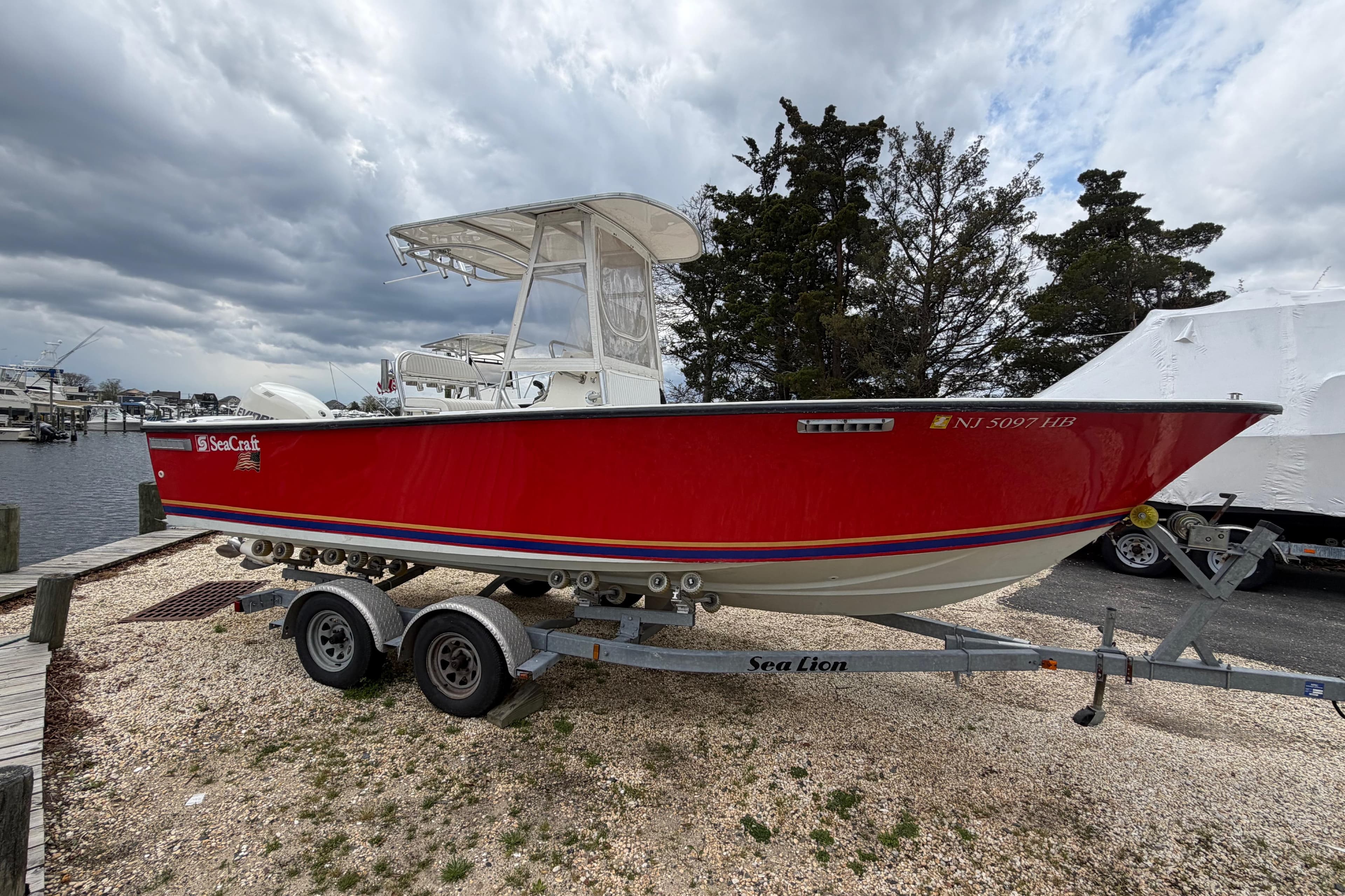 Red 1985 SeaCraft SC 23 Classic boat on trailer, parked near marina under cloudy sky.