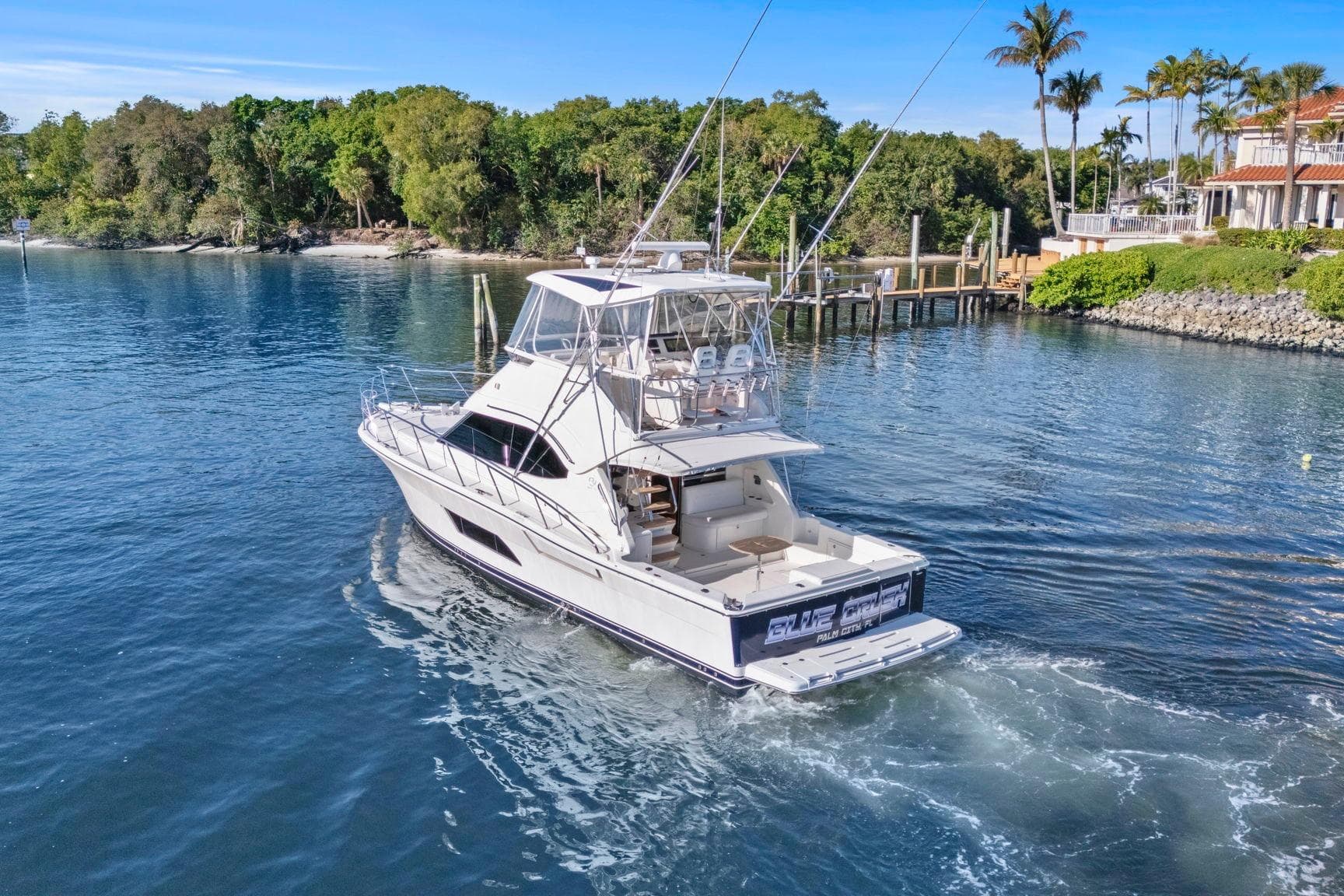 2016 Riviera 43 Open Flybridge yacht cruising near lush shoreline and docks.
