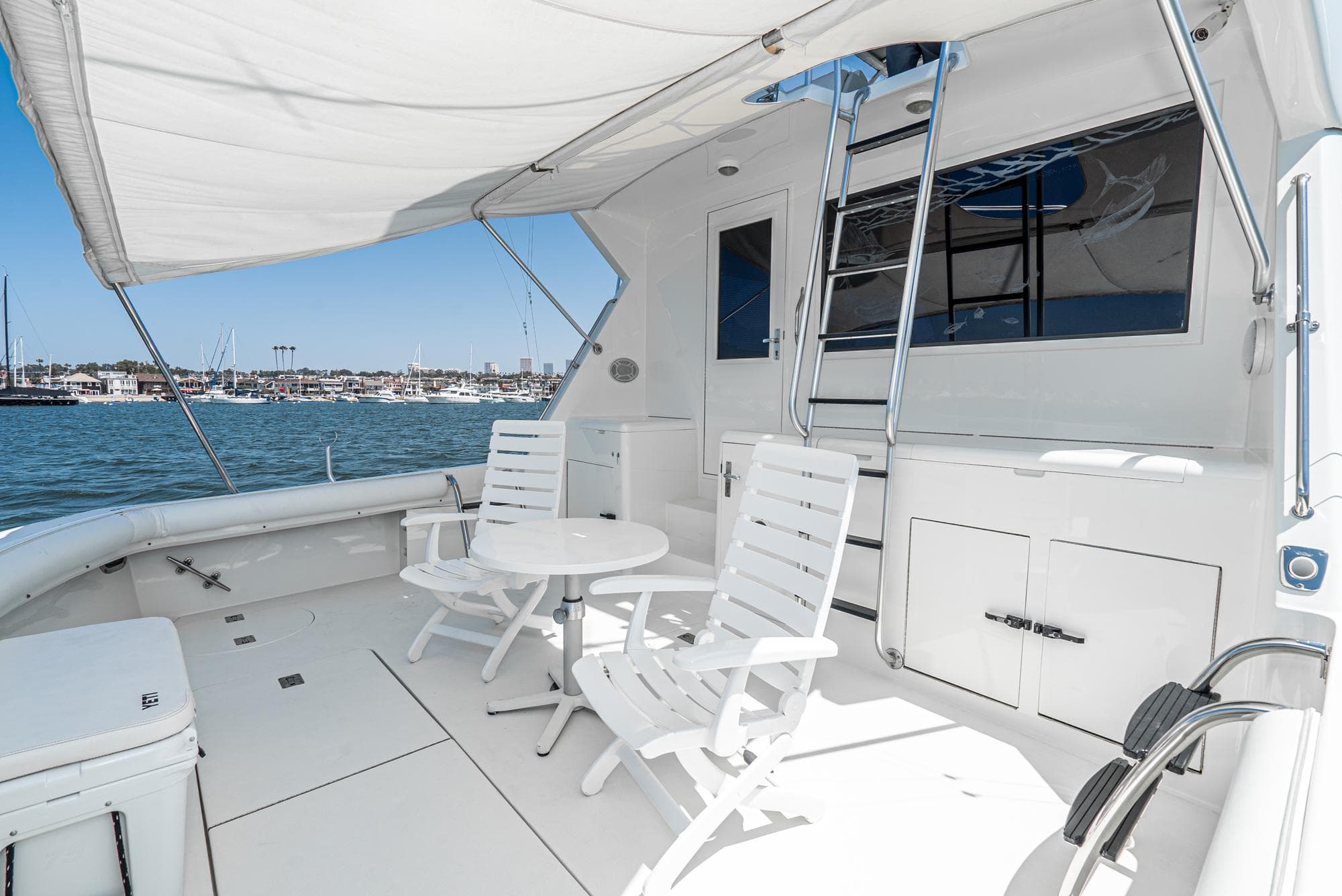 1990 Hatteras 58 Sportfish yacht deck with white chairs and table, overlooking marina.