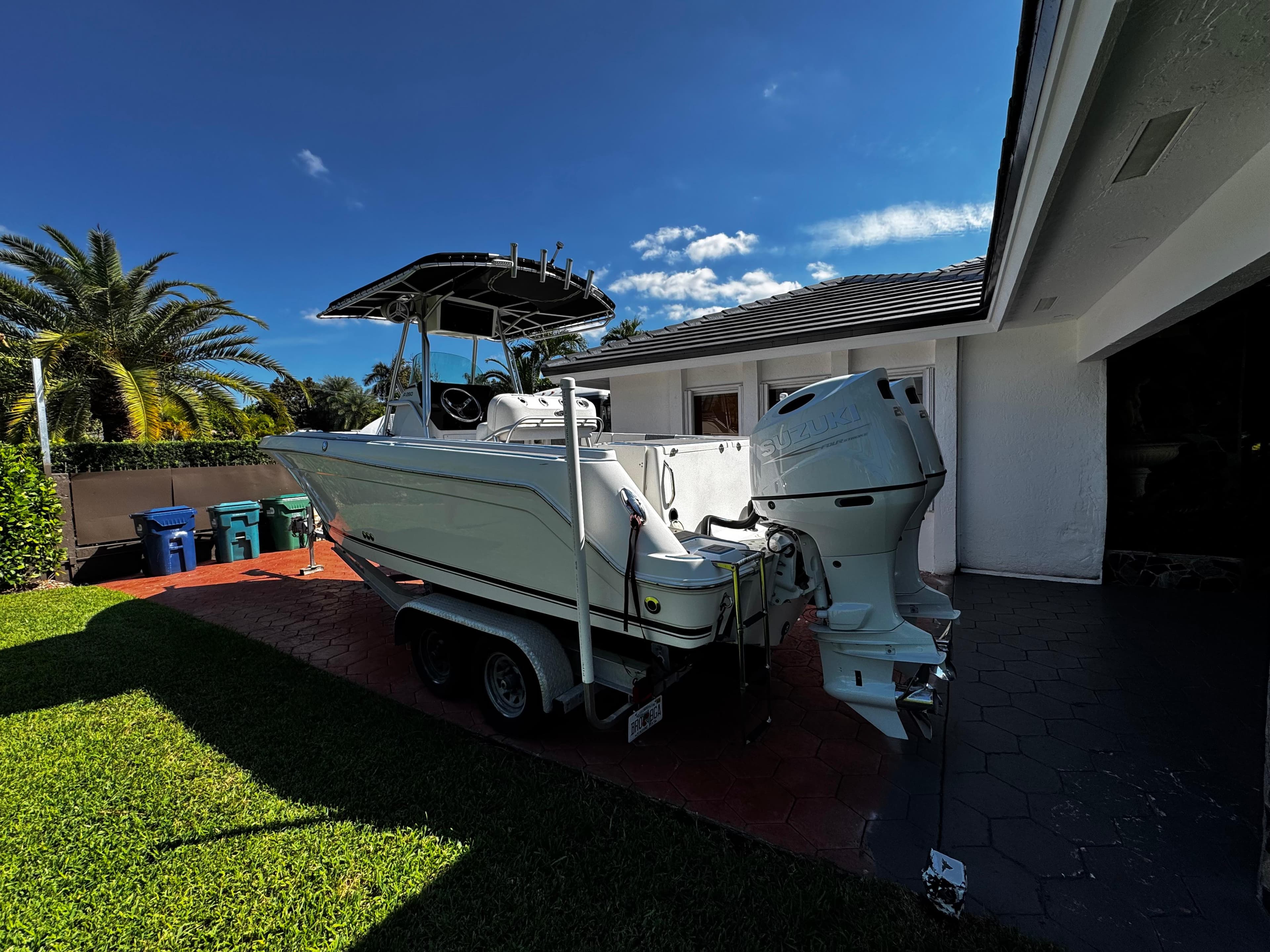 2004 Robalo R 260 boat on trailer beside house, under clear blue sky.