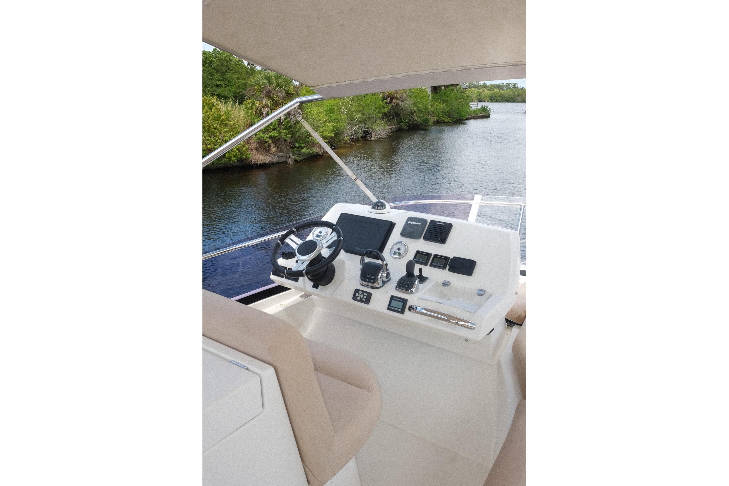 Helm of 2016 Prestige 500 yacht with modern controls, overlooking serene waterway.